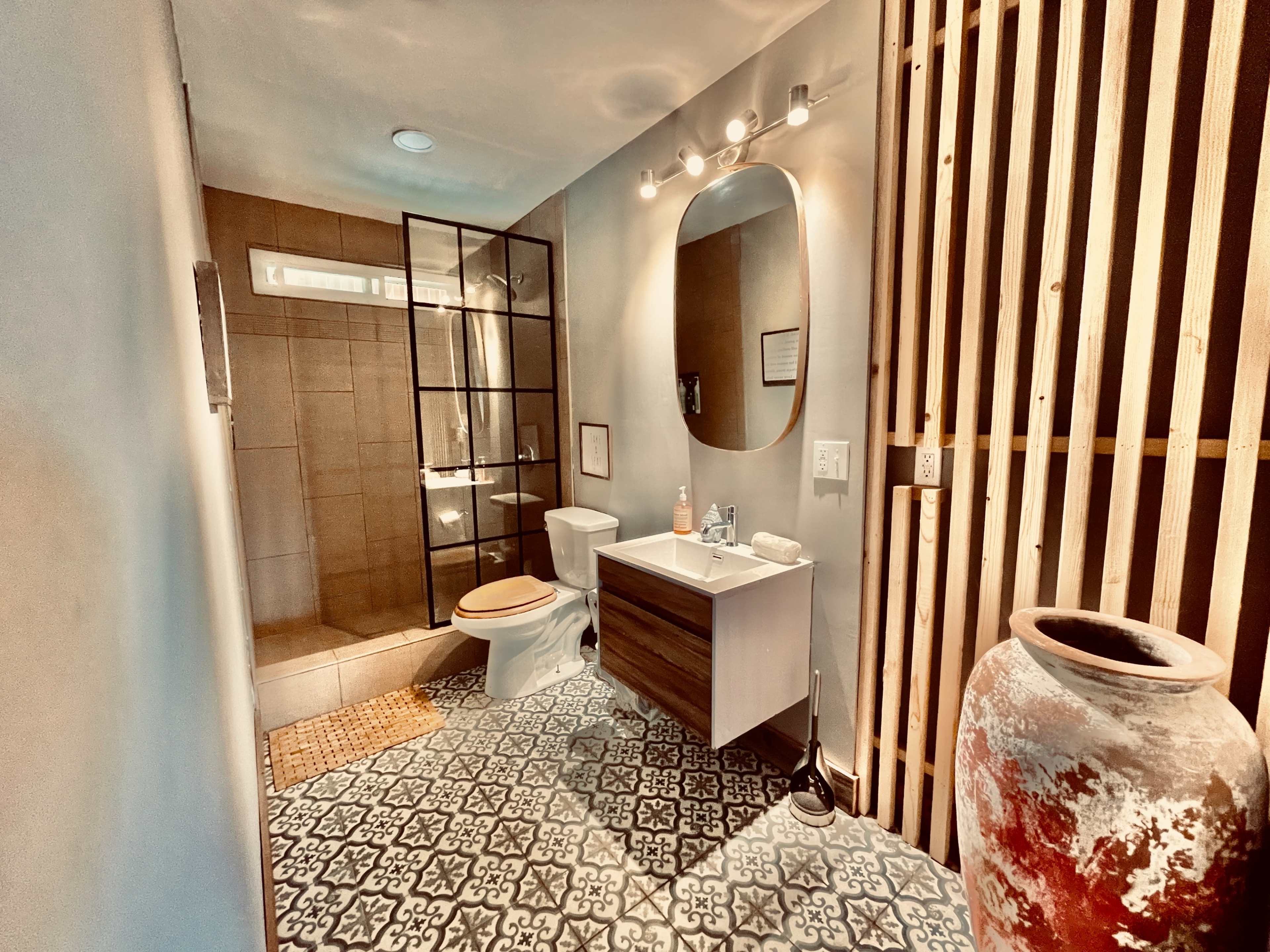 A modern bathroom featuring a glass shower, a toilet, a vanity with a sink, decorative floor tiles, and wooden accents on one wall.