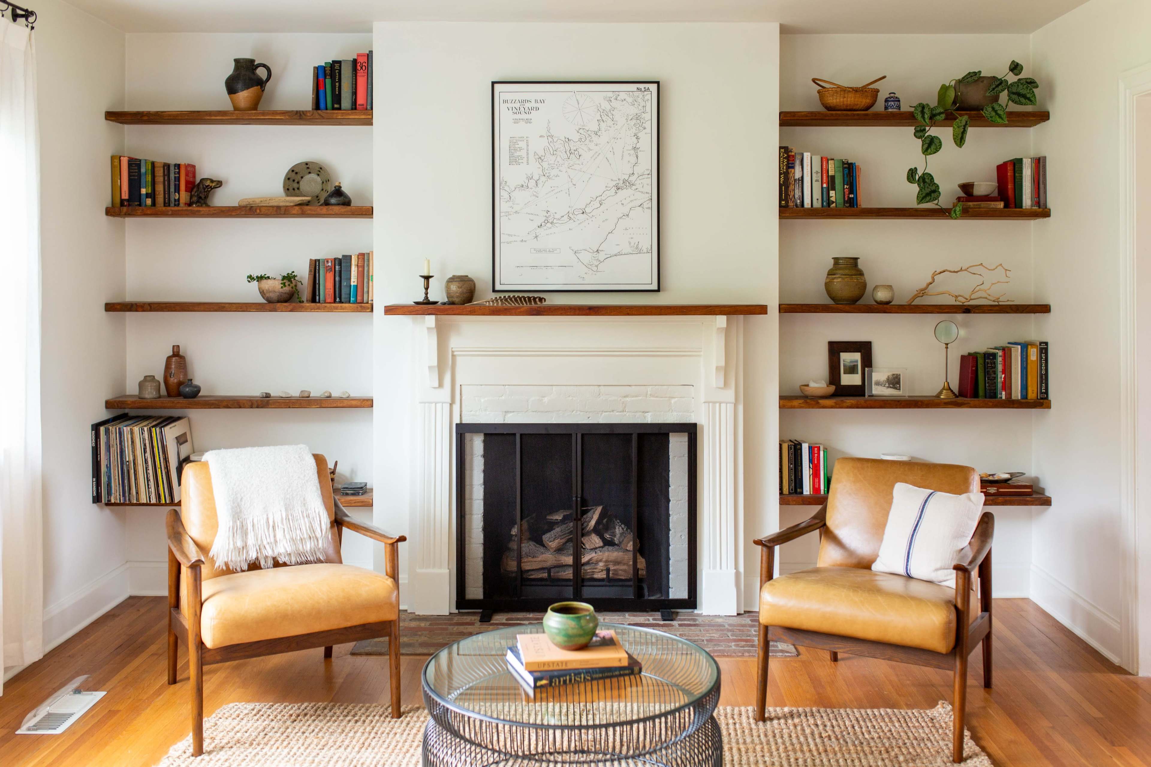 A cozy living room features two leather chairs facing a fireplace, with bookshelves filled with books and decorative items on either side.