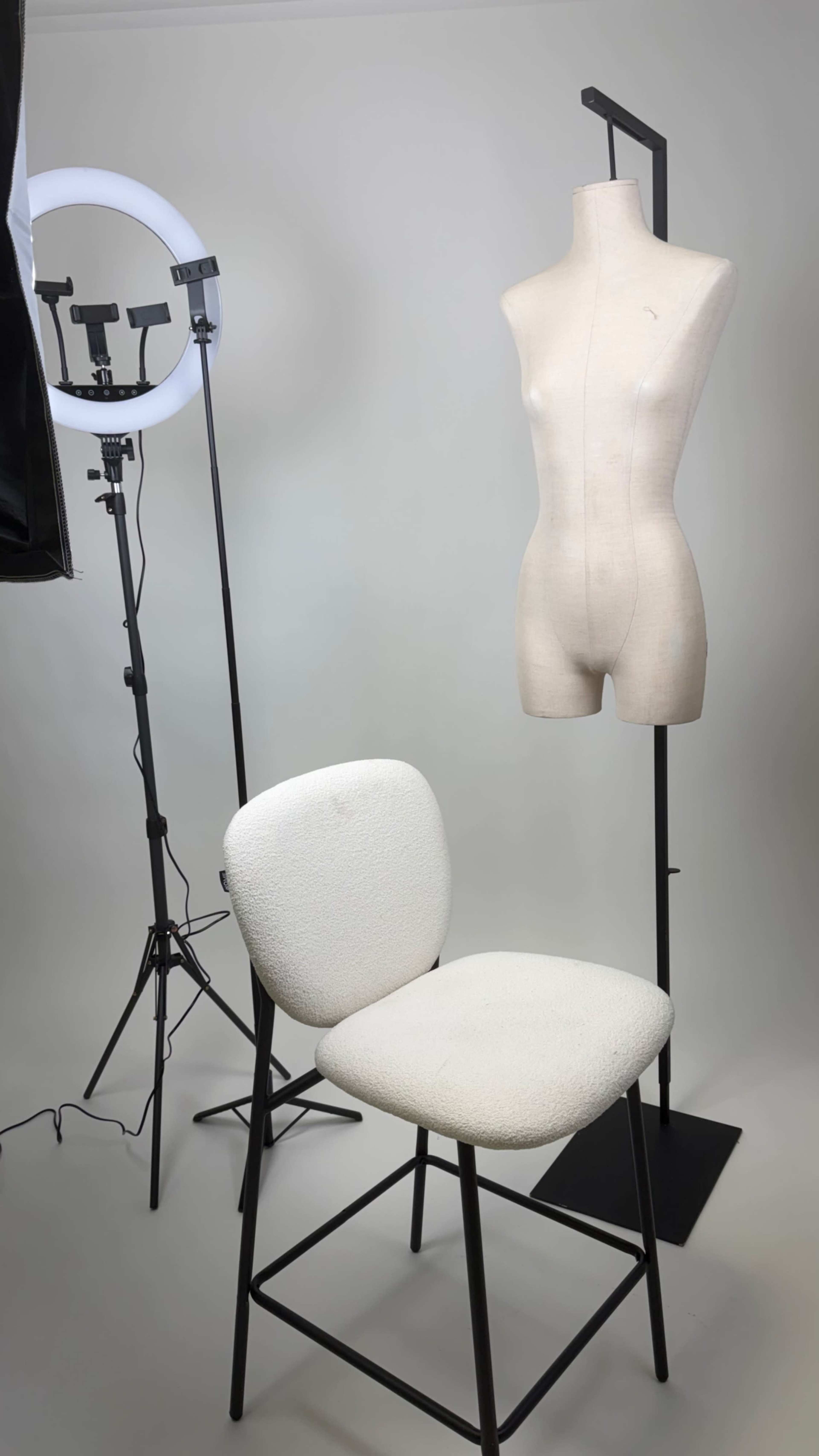 The image shows a white chair and a torso mannequin set up in front of a neutral background, accompanied by a ring light on a stand.