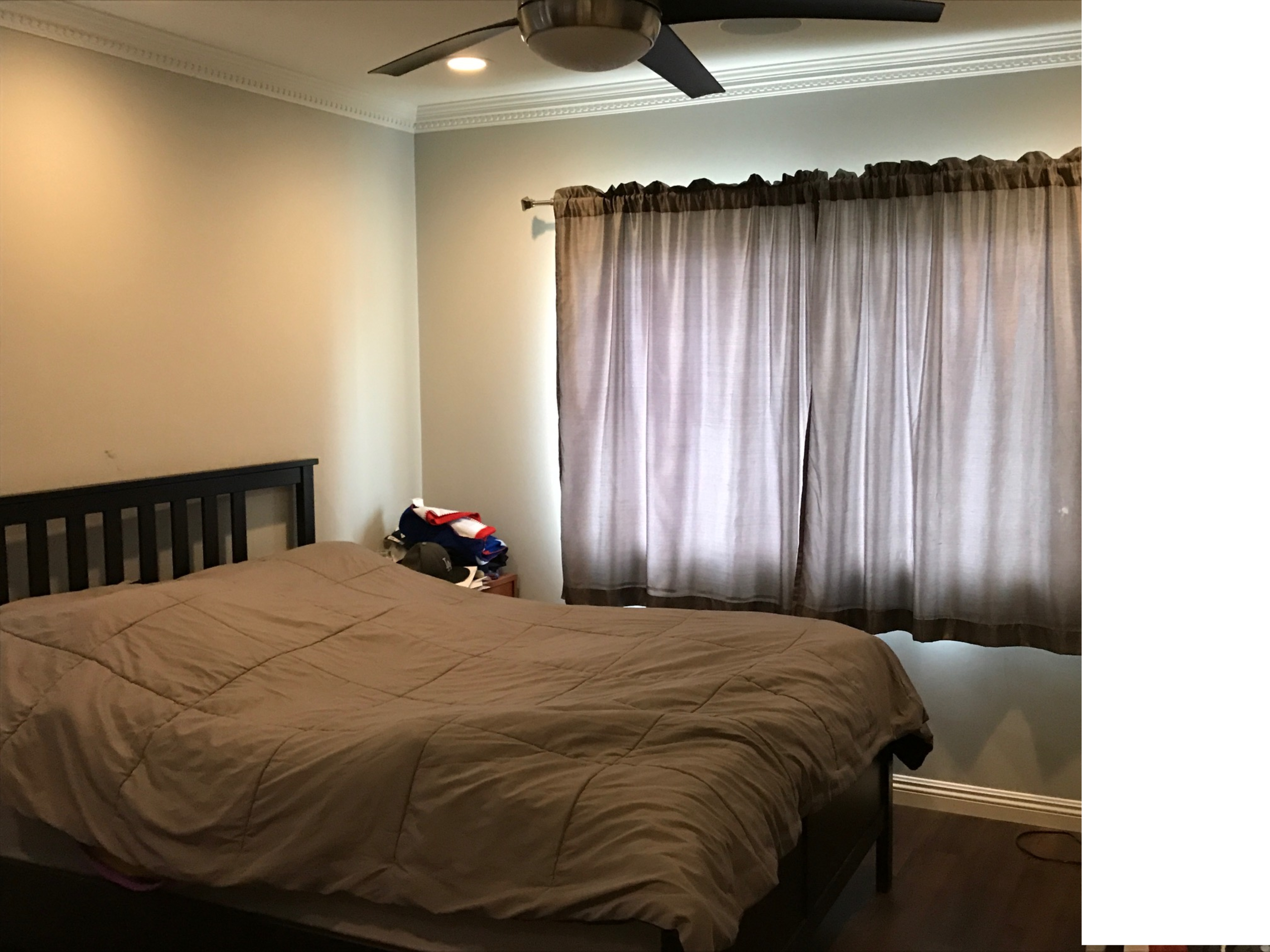 A bedroom with a bed, a ceiling fan, and a large window covered by curtains.