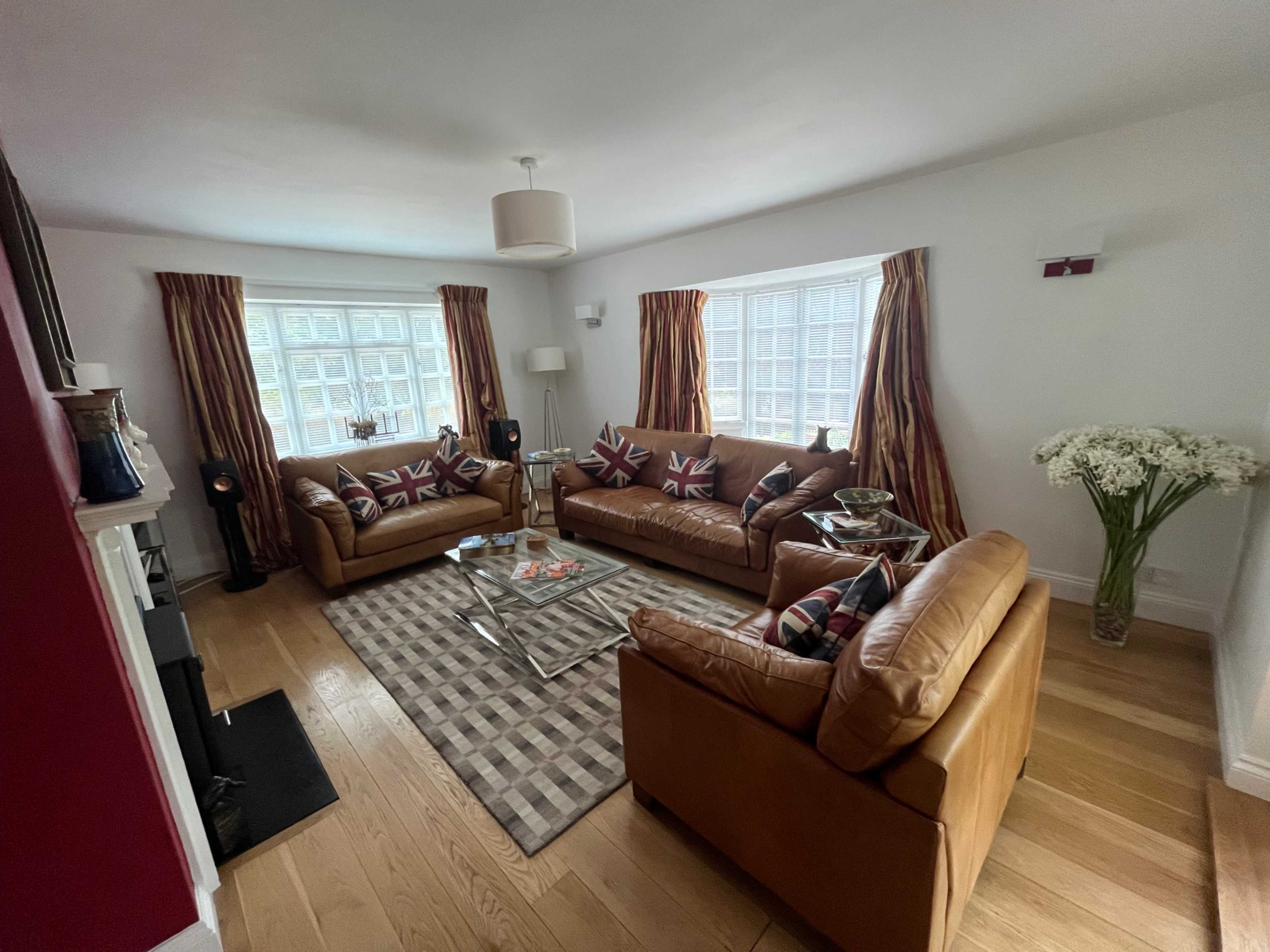 A living room with brown leather sofas, a patterned rug, and decorative windows, alongside a coffee table and a large bouquet of flowers.