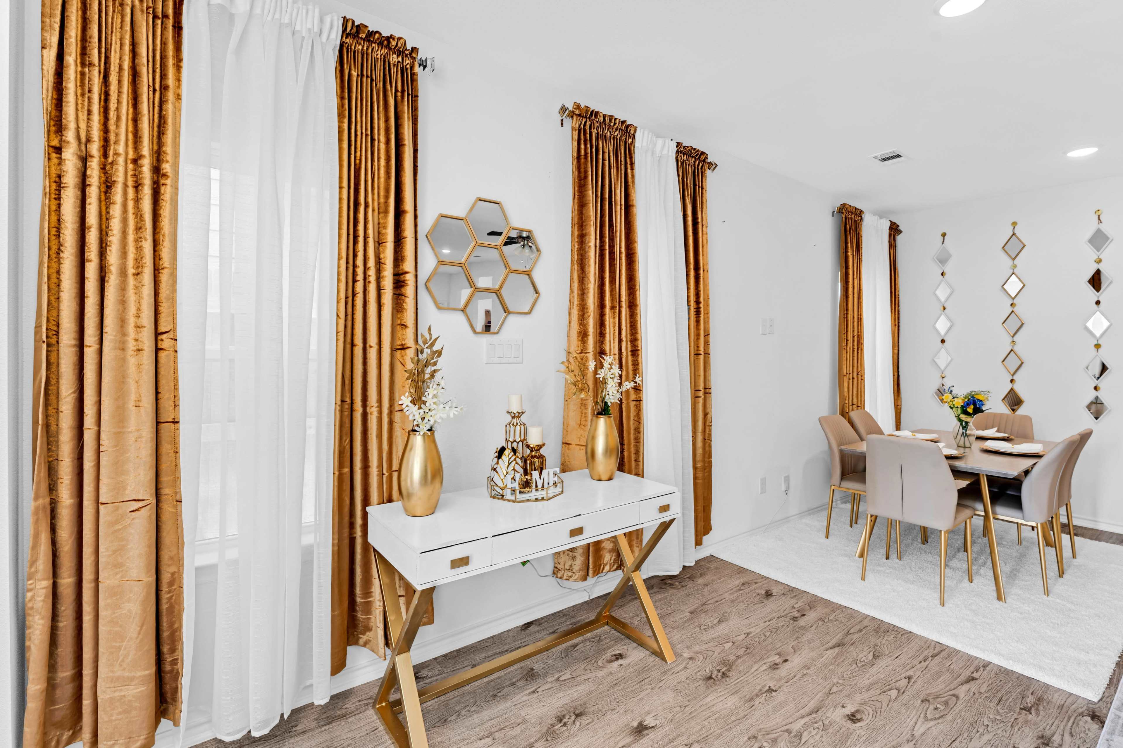 A dining area with a white table and beige chairs, surrounded by gold-accented decor and curtains, alongside a decorative mirror.