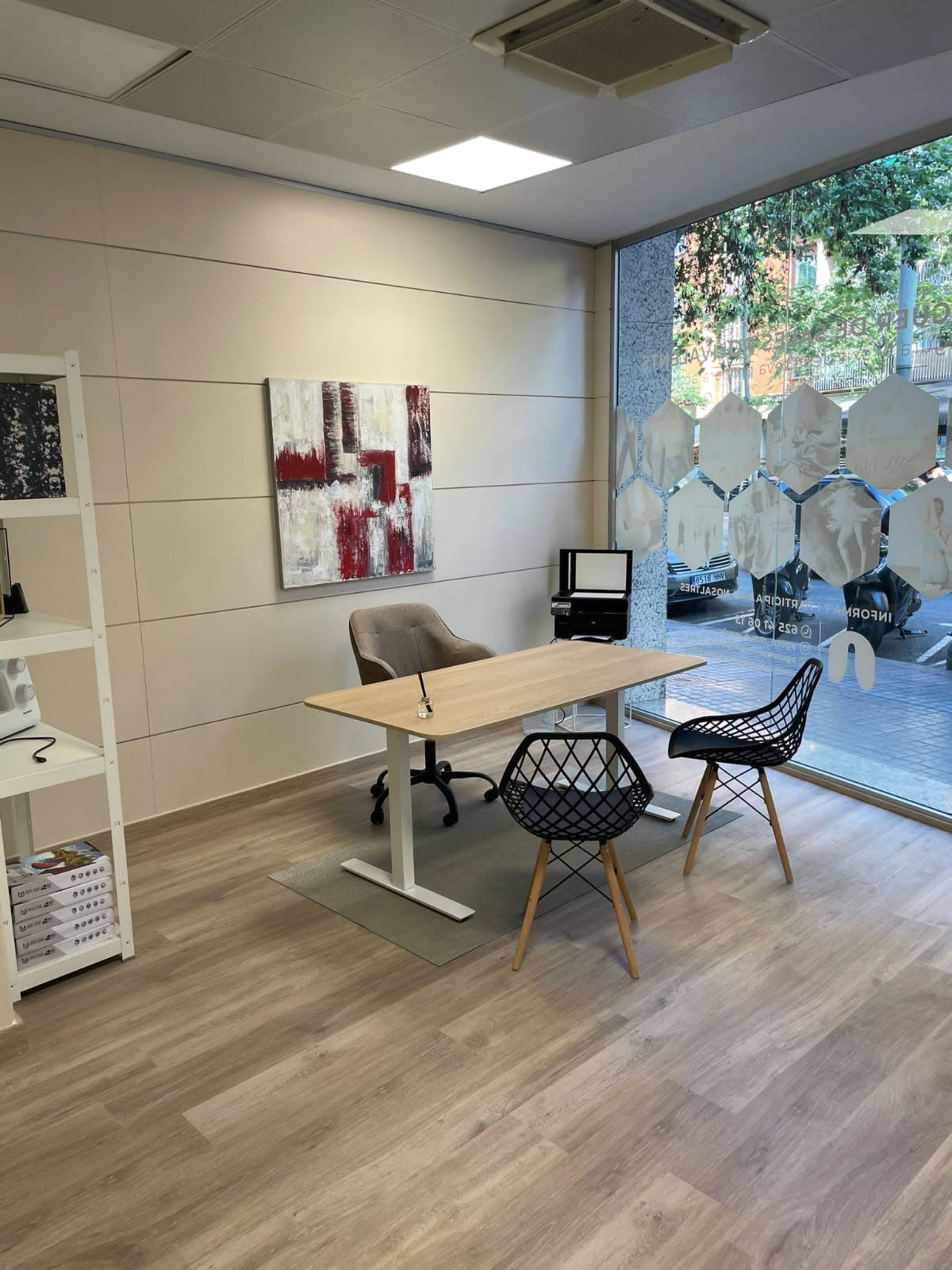 A modern office space with a wooden desk and two chairs, surrounded by light-colored walls and large windows.
