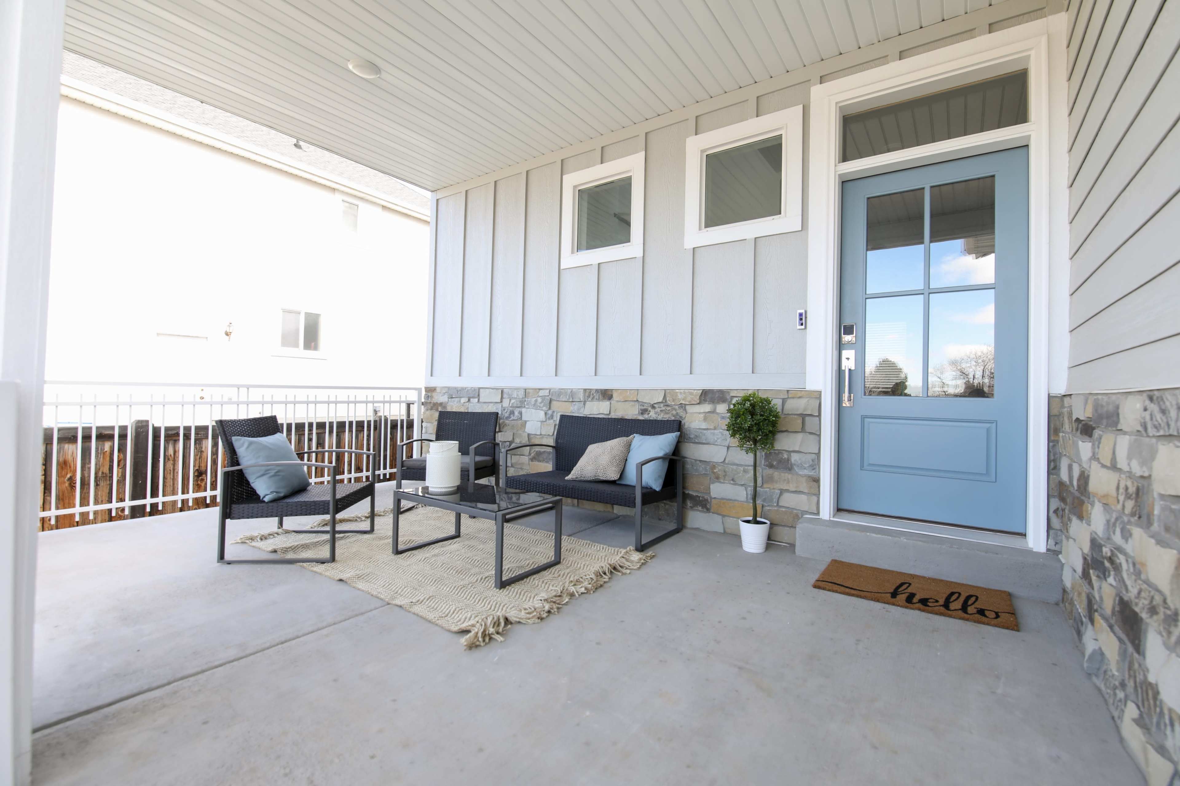 A covered porch featuring a seating area with two chairs, a small table, a welcome mat, and a decorative plant by the door.