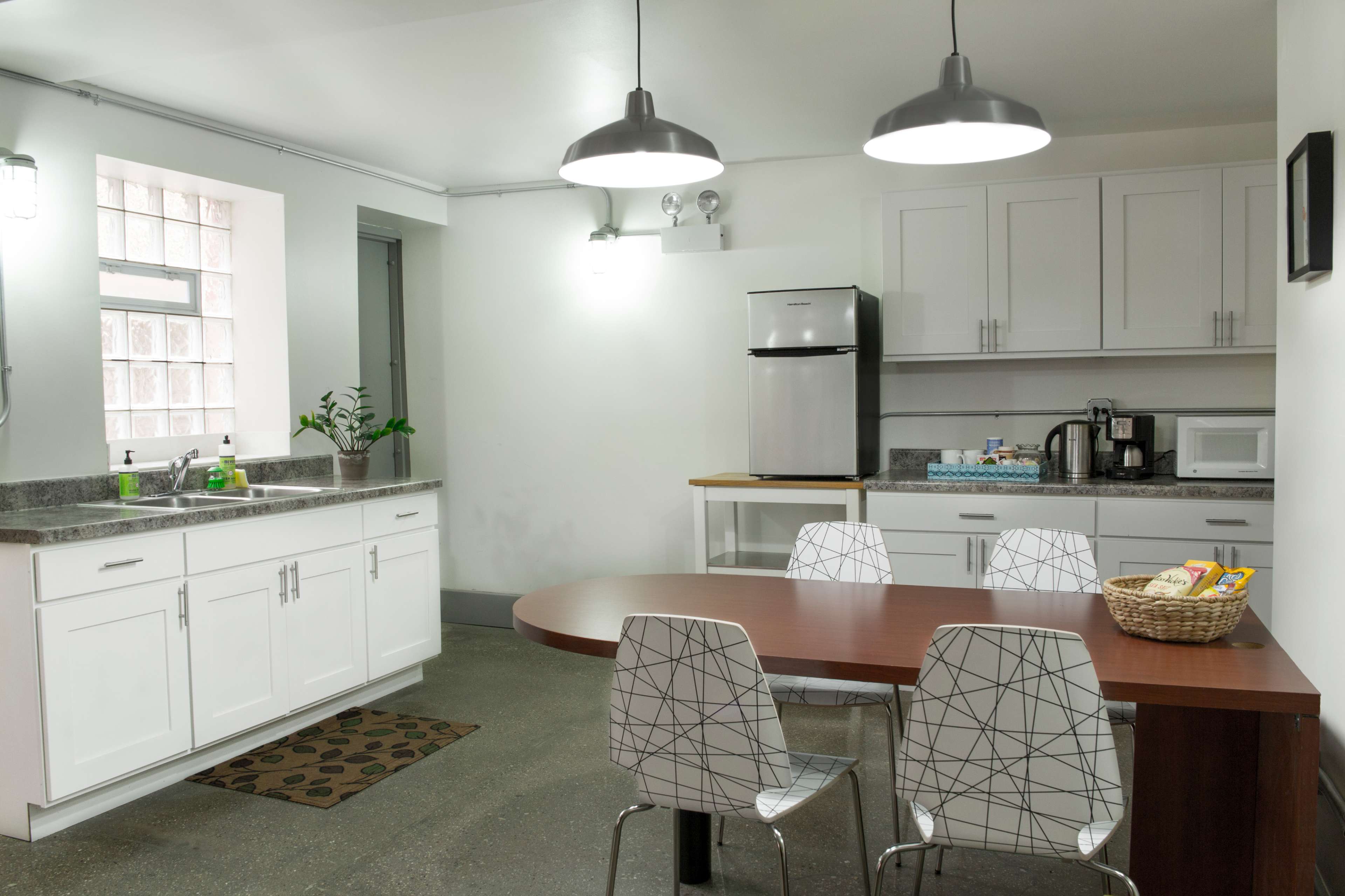 A modern kitchen features white cabinetry, stainless steel appliances, and a circular wooden dining table surrounded by four clear plastic chairs.
