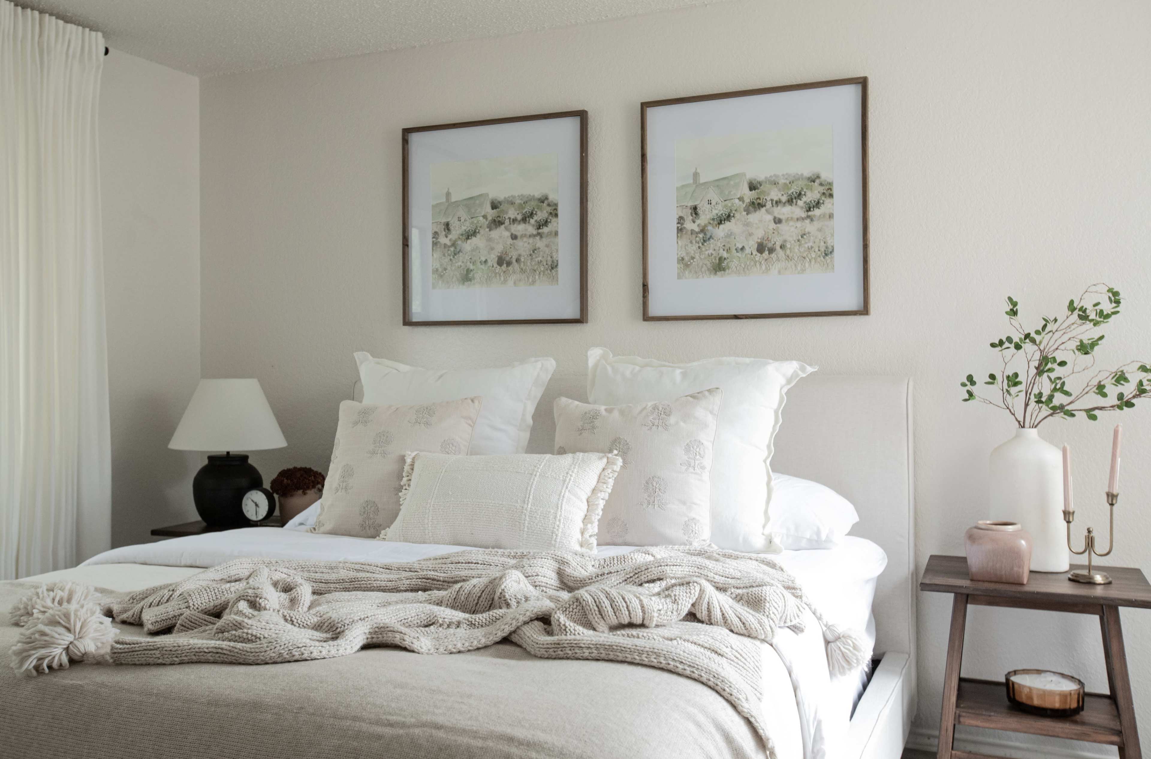 A neatly arranged bedroom features a bed with decorative pillows, a soft throw blanket, and framed artwork on the walls.