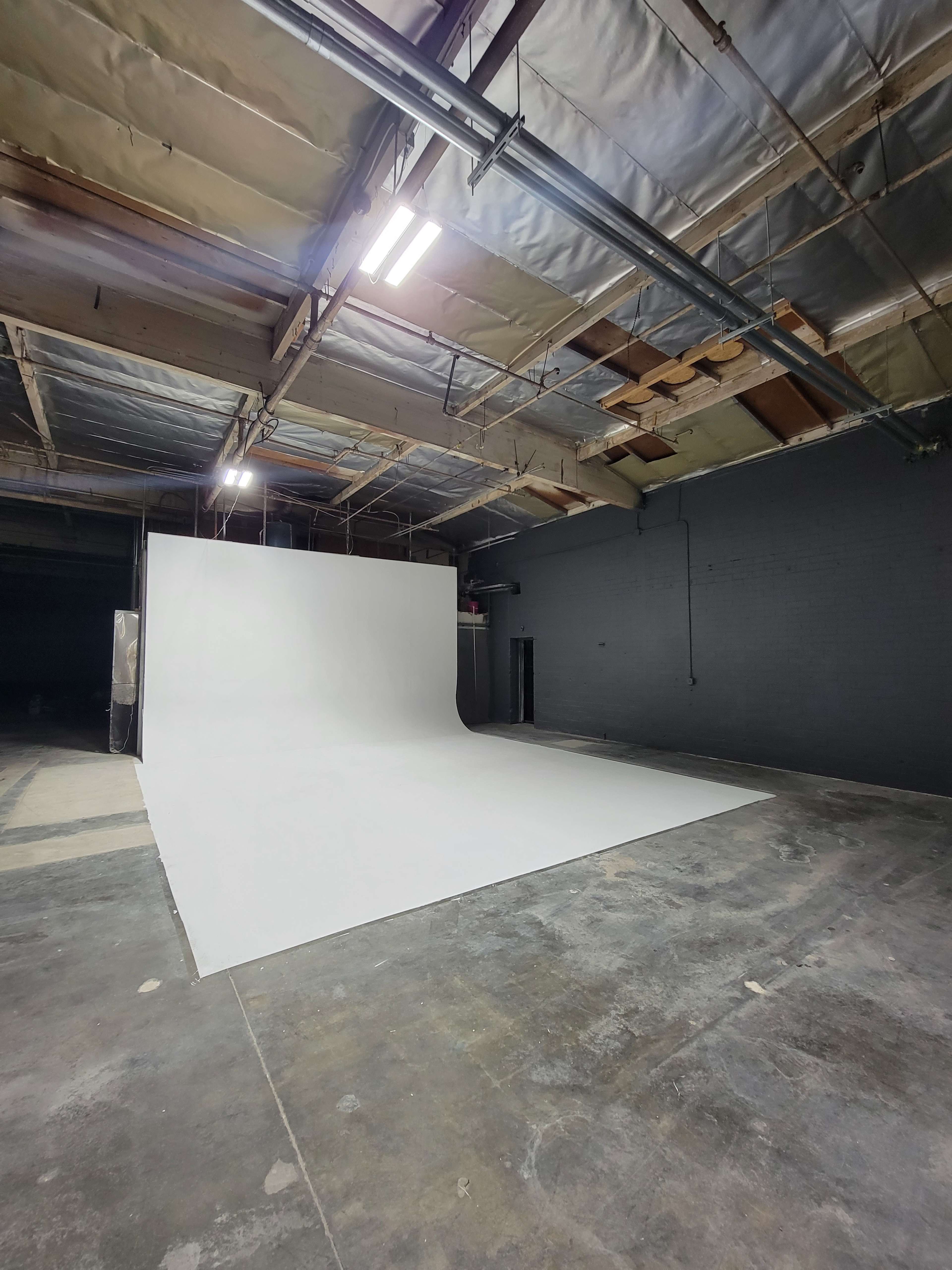 The image shows a spacious indoor studio with a large white backdrop and concrete flooring.