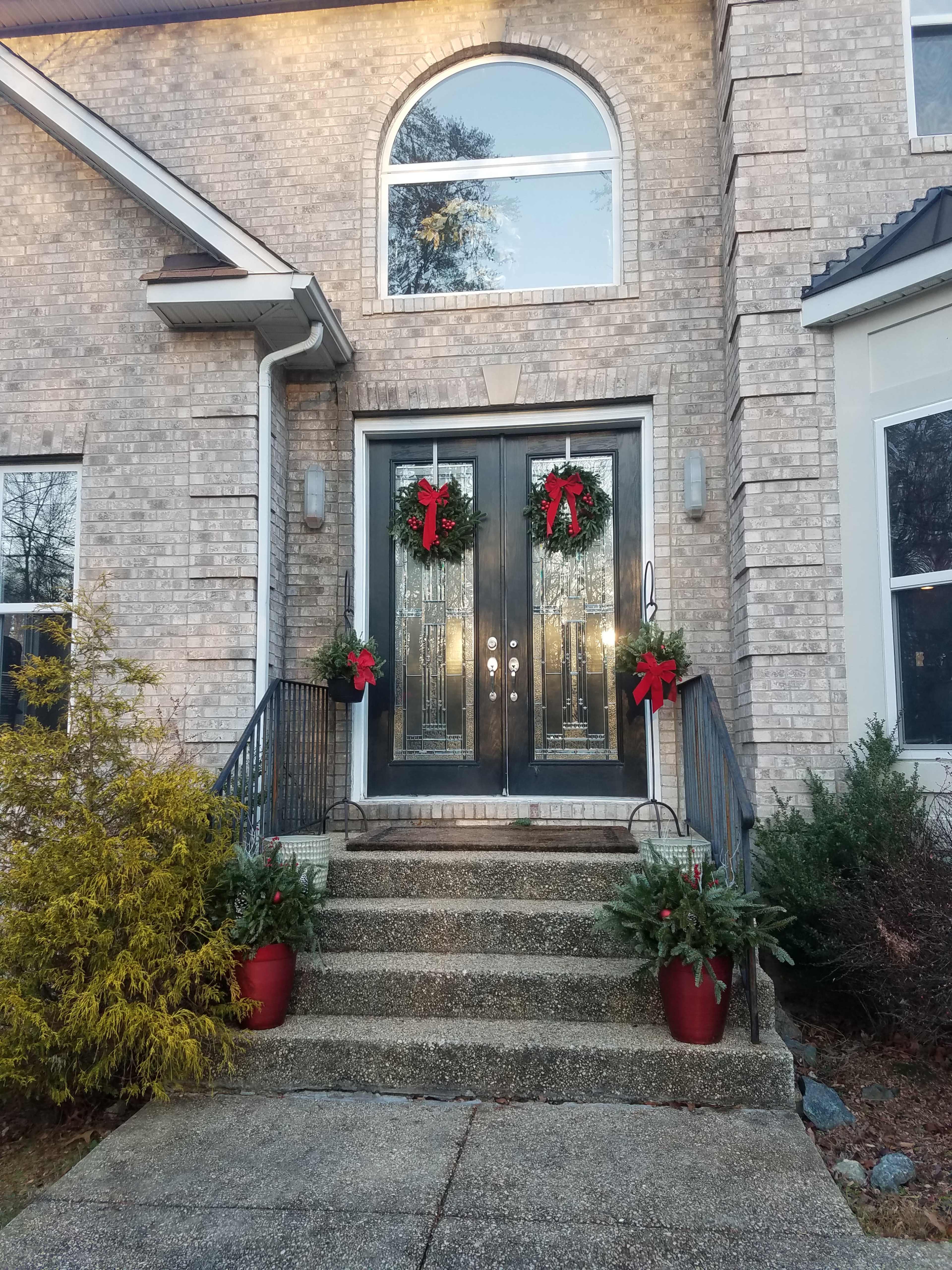 A front entrance features double doors adorned with wreaths and red bows, flanked by potted greenery and a stone stairway.