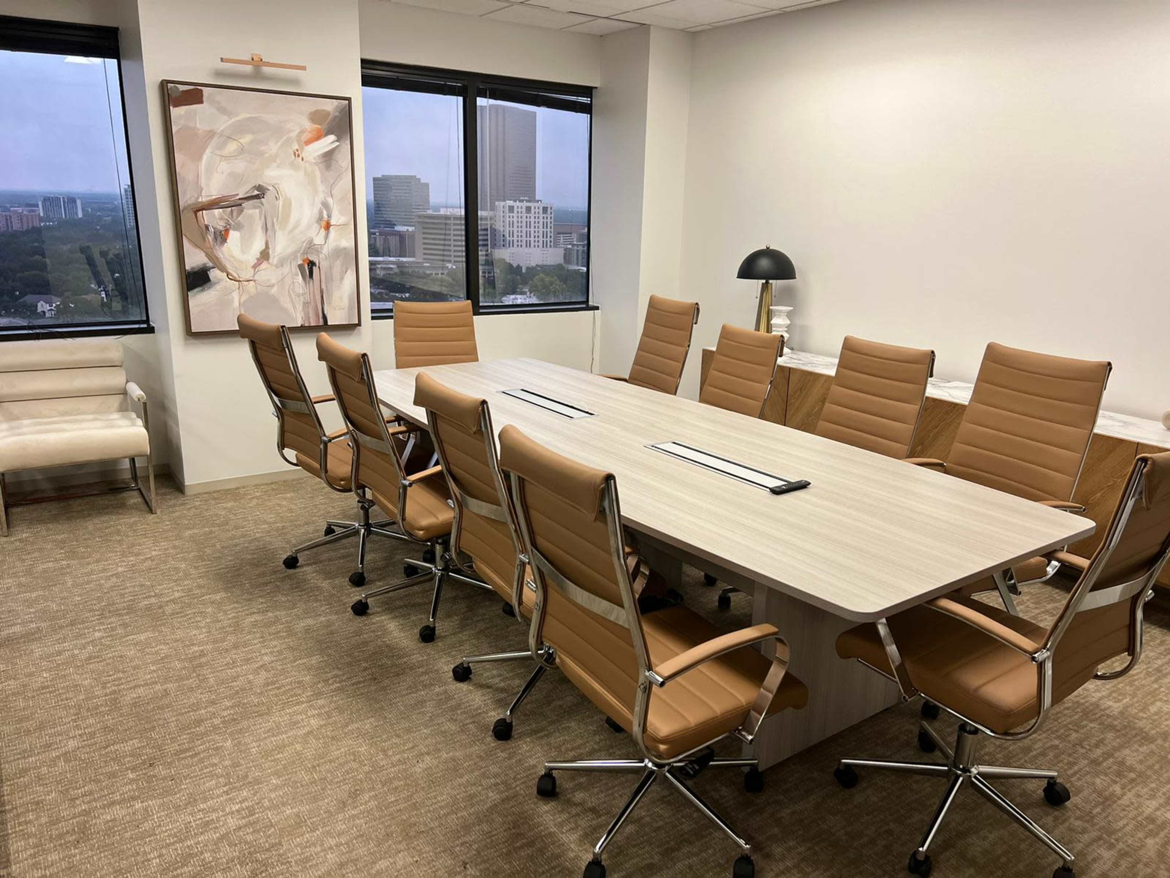 A modern conference room featuring a long wooden table surrounded by eight leather chairs, with large windows overlooking a cityscape.