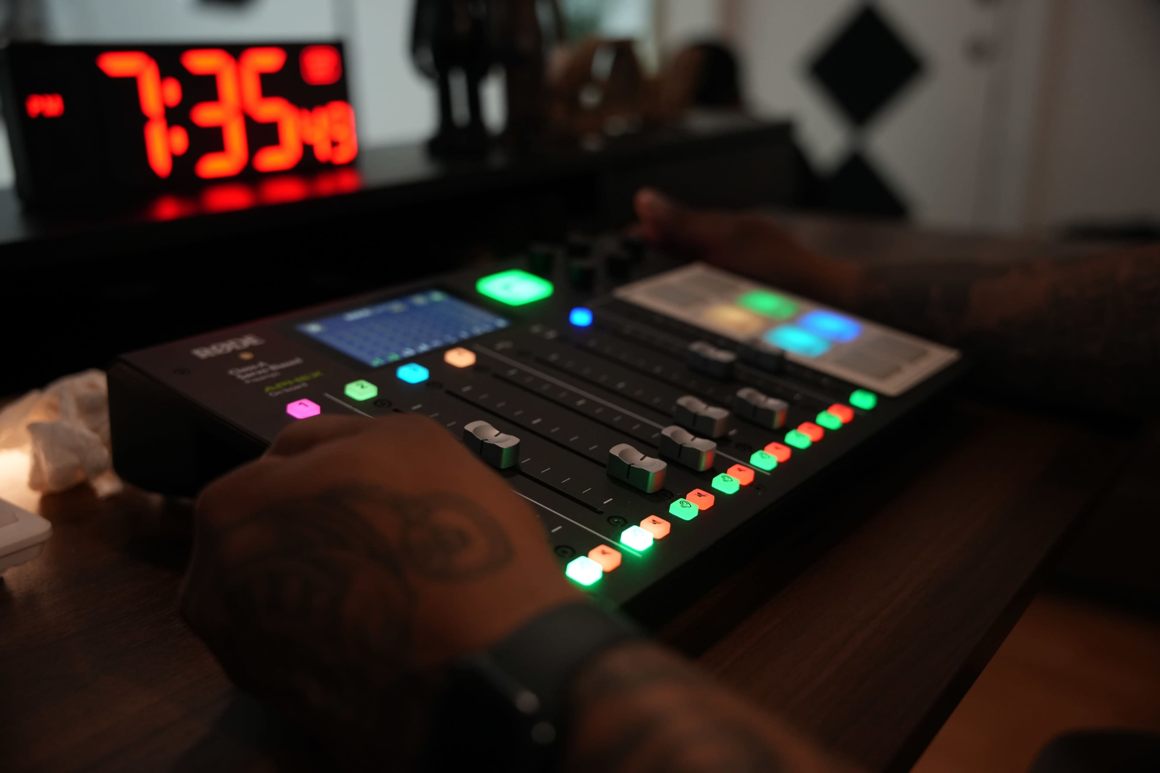 A person is adjusting the sound levels on a digital audio mixer with colorful LED indicators, while a clock displays 7:35 PM in the background.