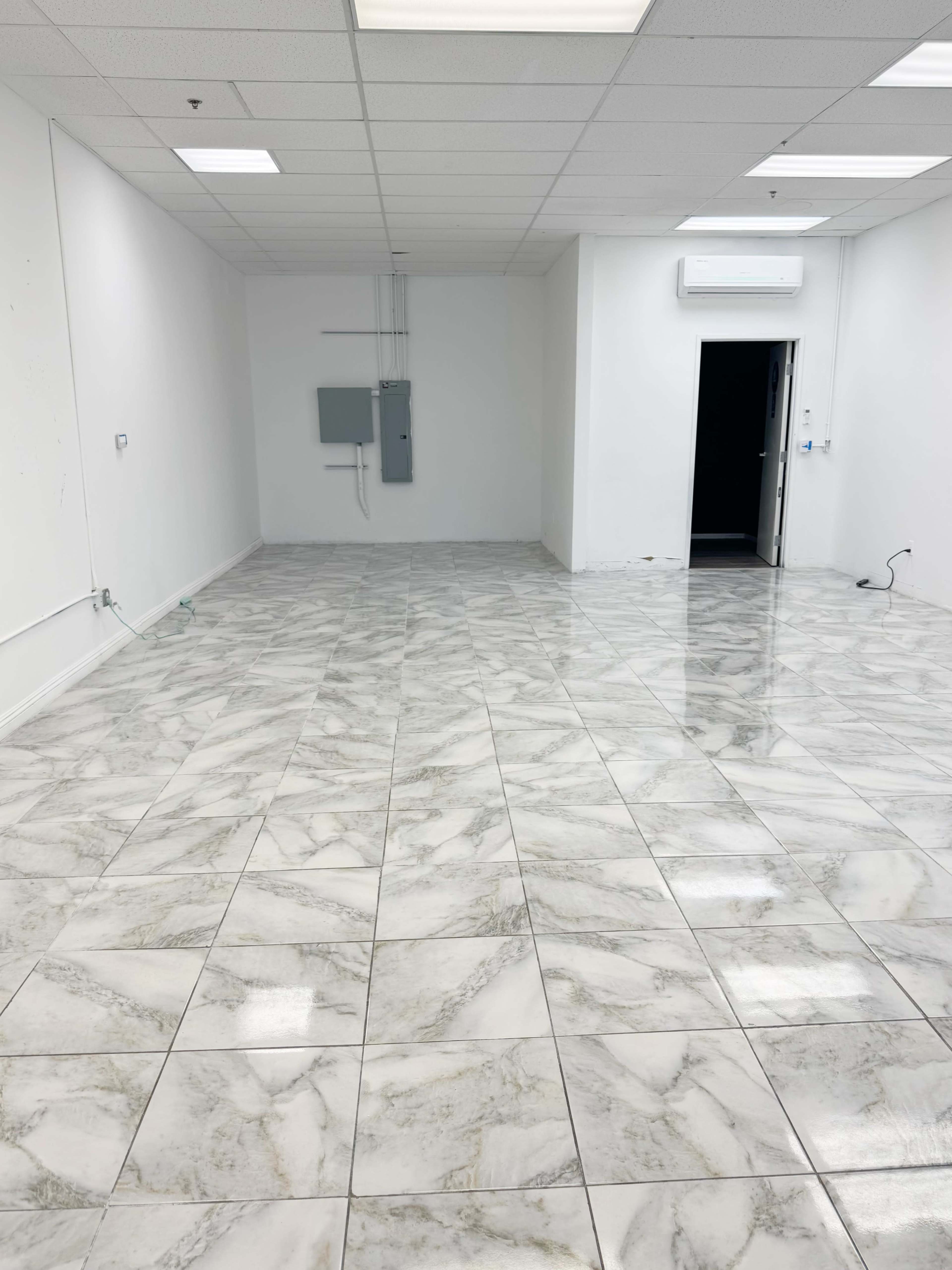 The image shows a large, empty room with glossy marble floor tiles, white walls, and a door leading to another space.