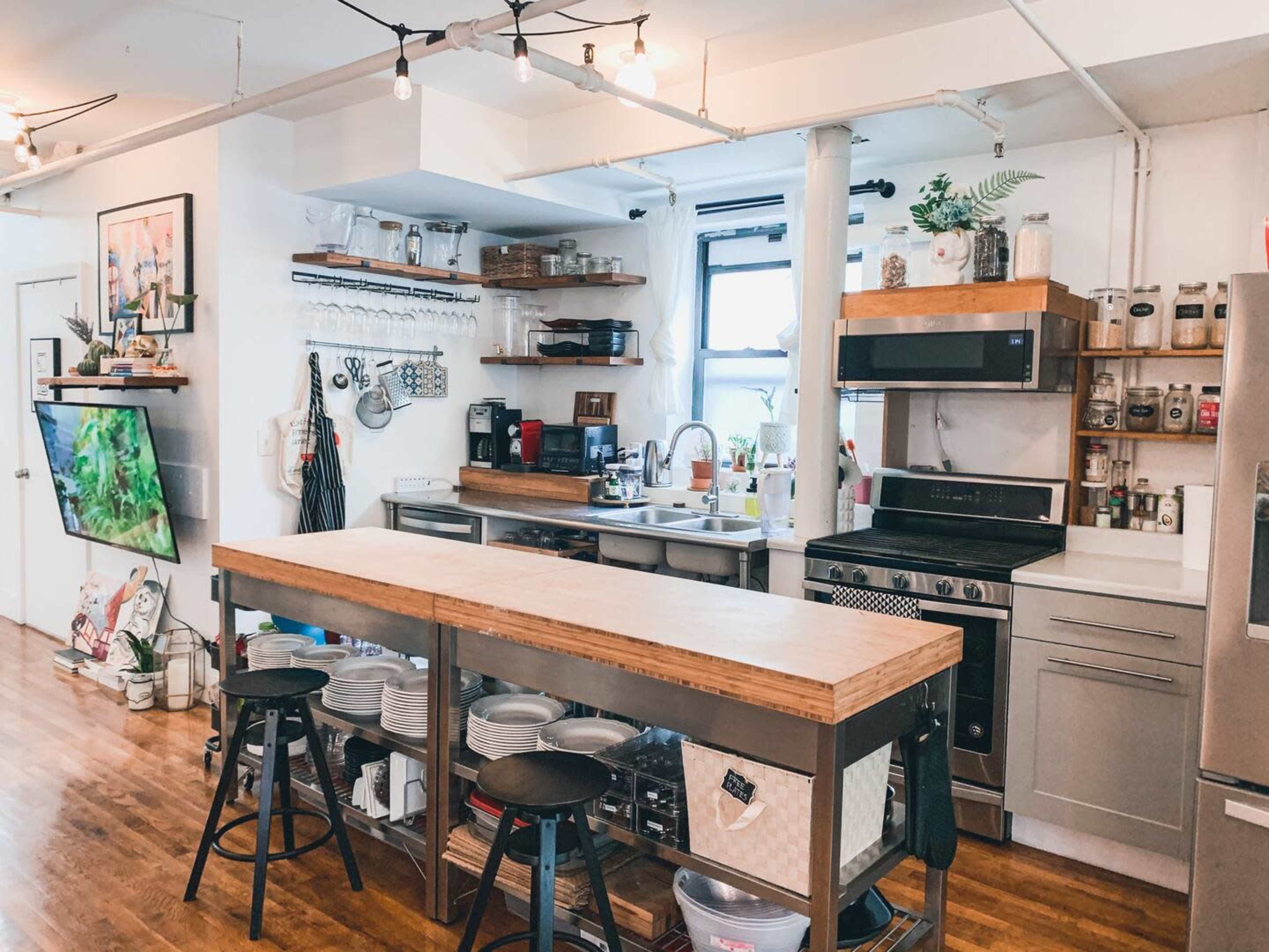 A modern kitchen with a central wooden island, open shelving, stainless steel appliances, and a seating area with black stools.