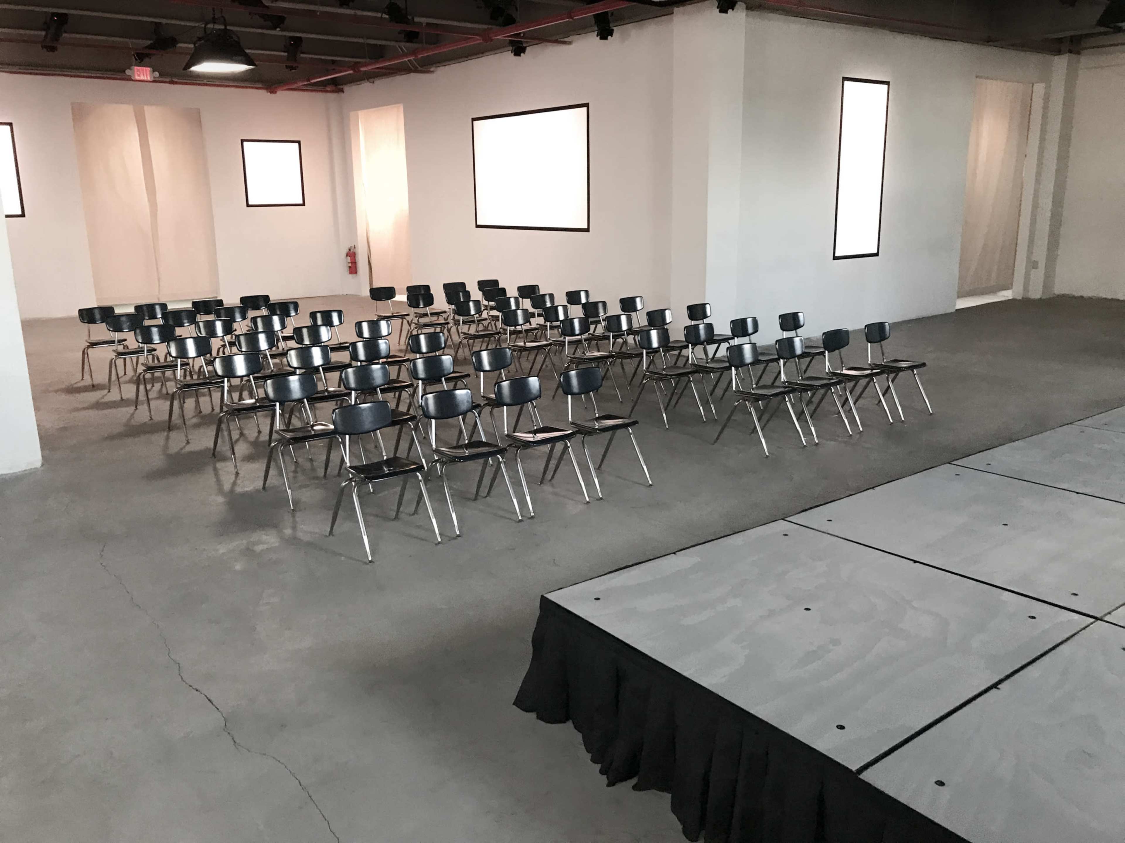 A spacious room arranged with rows of black chairs facing a raised stage covered with a black tablecloth.