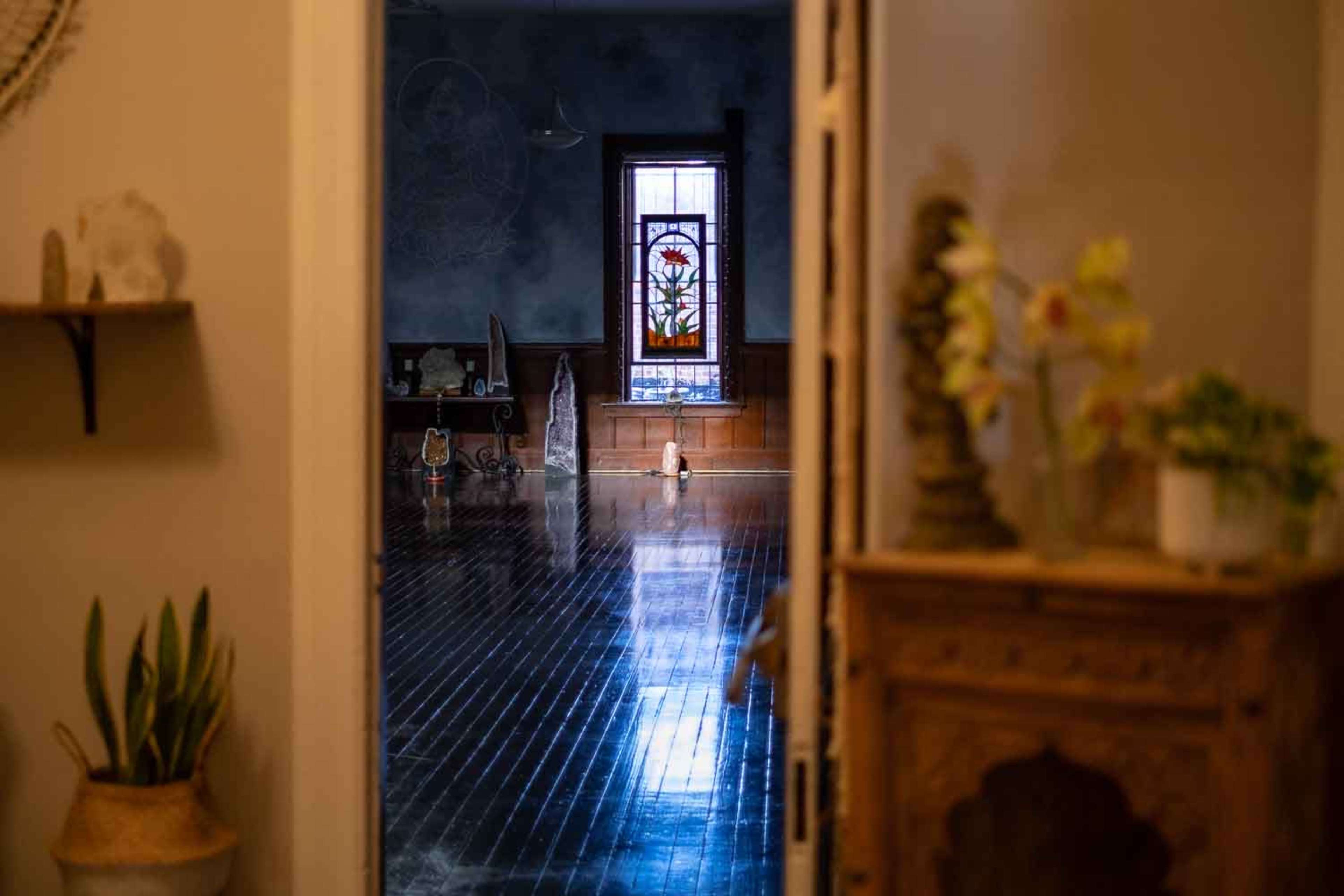 A doorway frames a view of a spacious room featuring a colorful stained glass window and polished wooden floors.