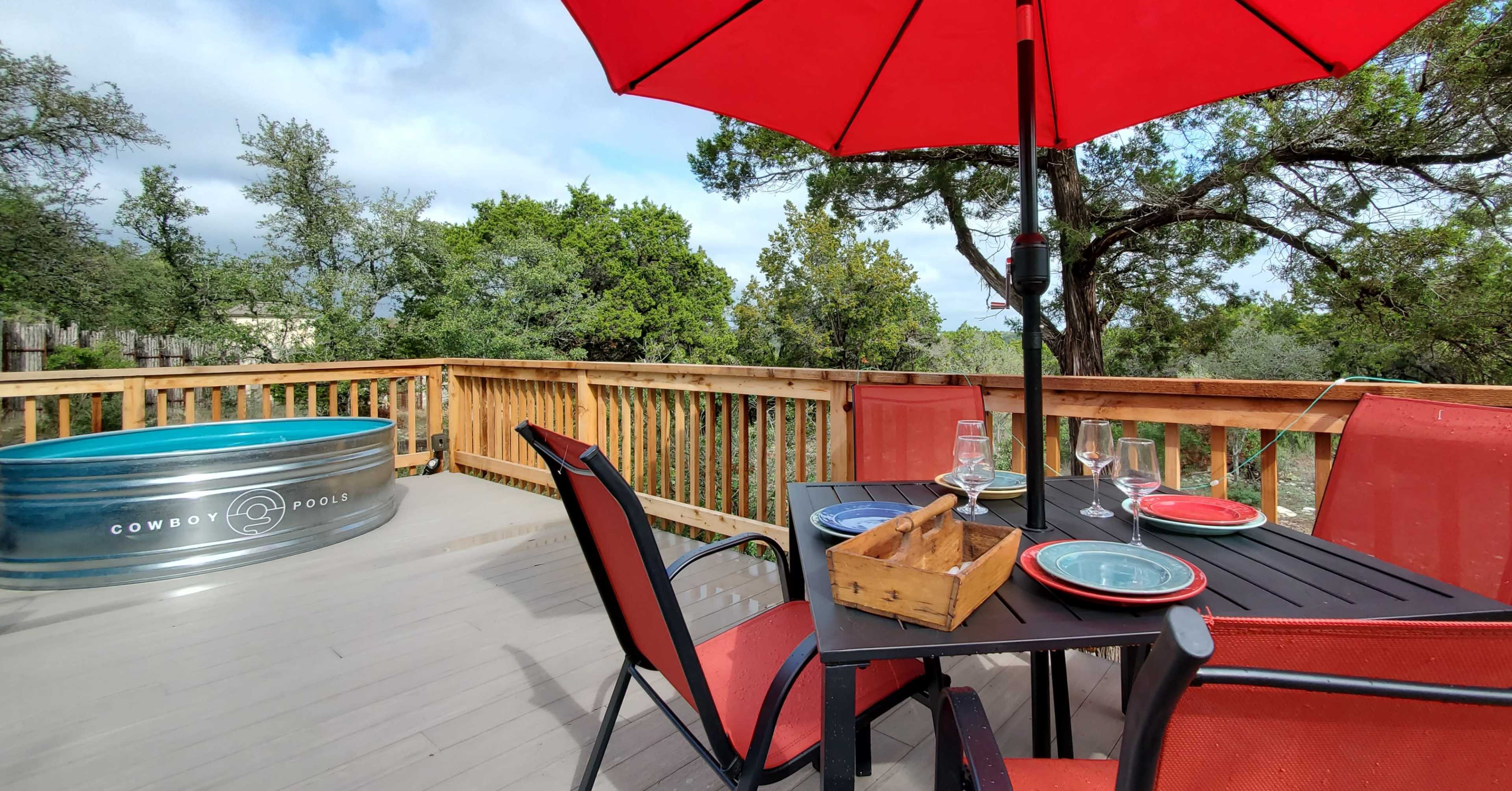 A wooden deck features a dining table set with dishes and glasses, an umbrella providing shade, and a cowboy-themed pool nearby.