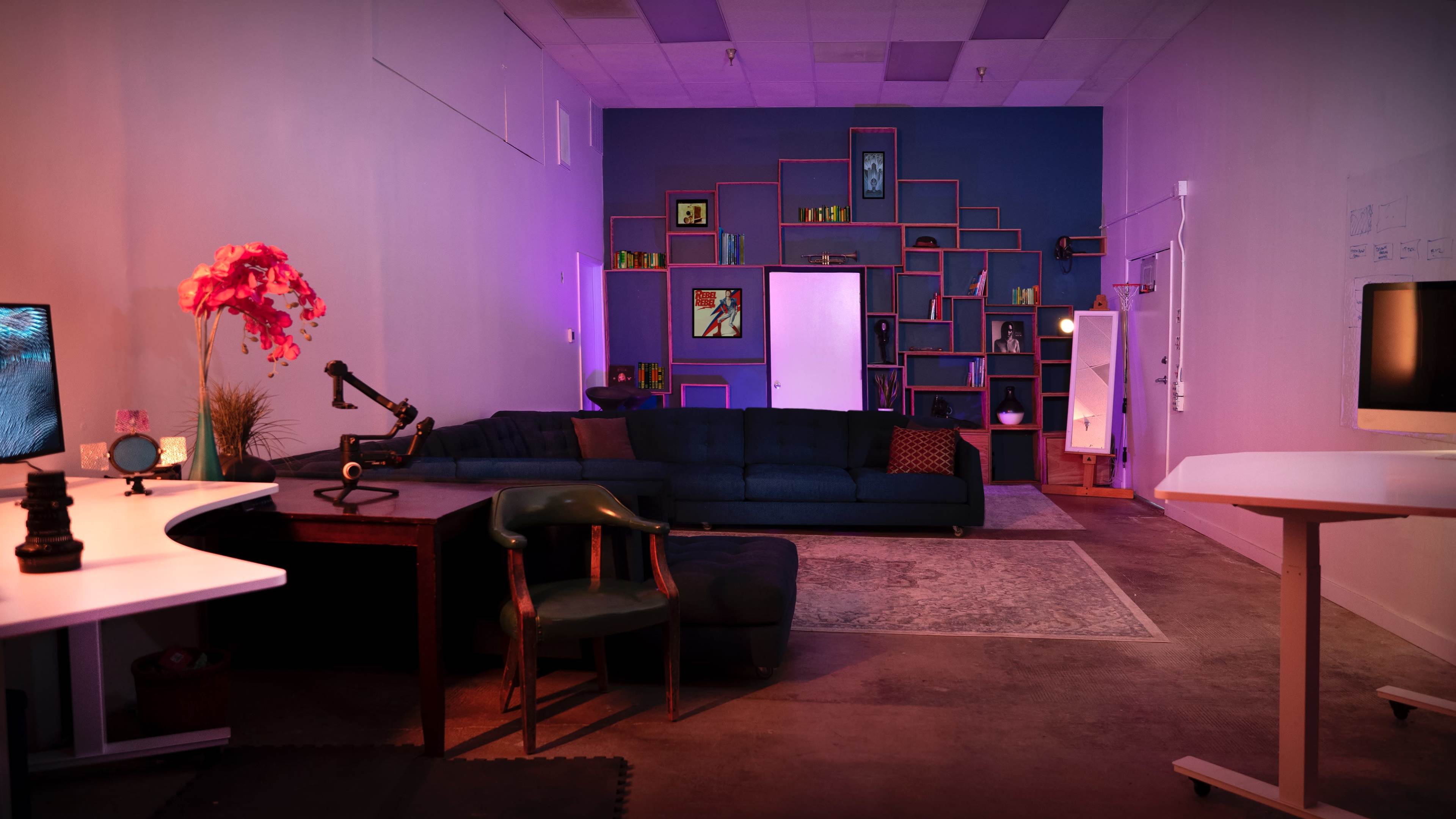 A modern interior space featuring a blue sofa, a desk with a green chair, and a colorful shelving unit against the wall.