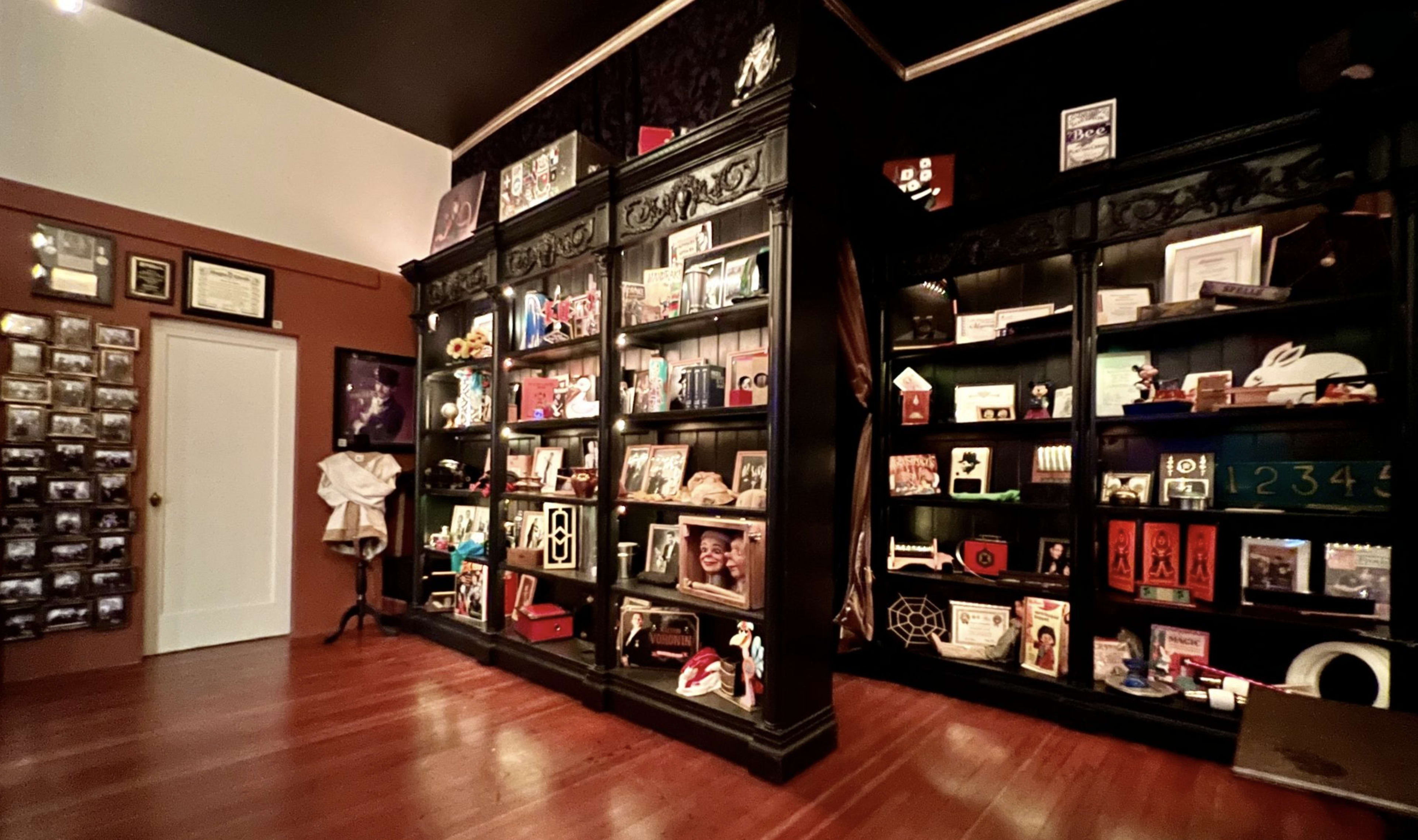 A cozy room featuring dark wooden shelves filled with various framed photos, memorabilia, and decorative items, alongside a wall adorned with many small pictures and certificates.