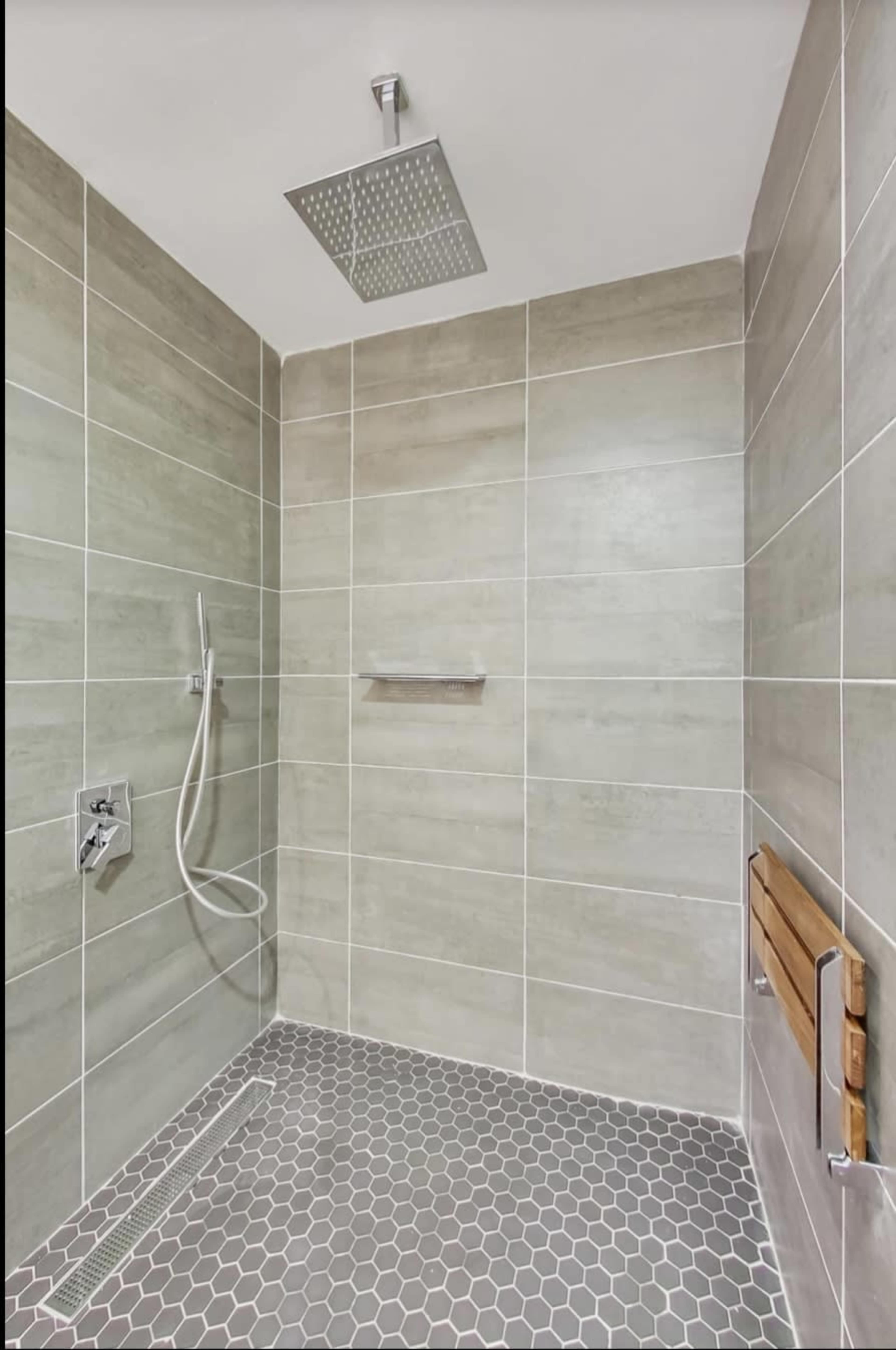 A modern shower space with gray tiled walls, a hexagonal tiled floor, and a rainfall showerhead.