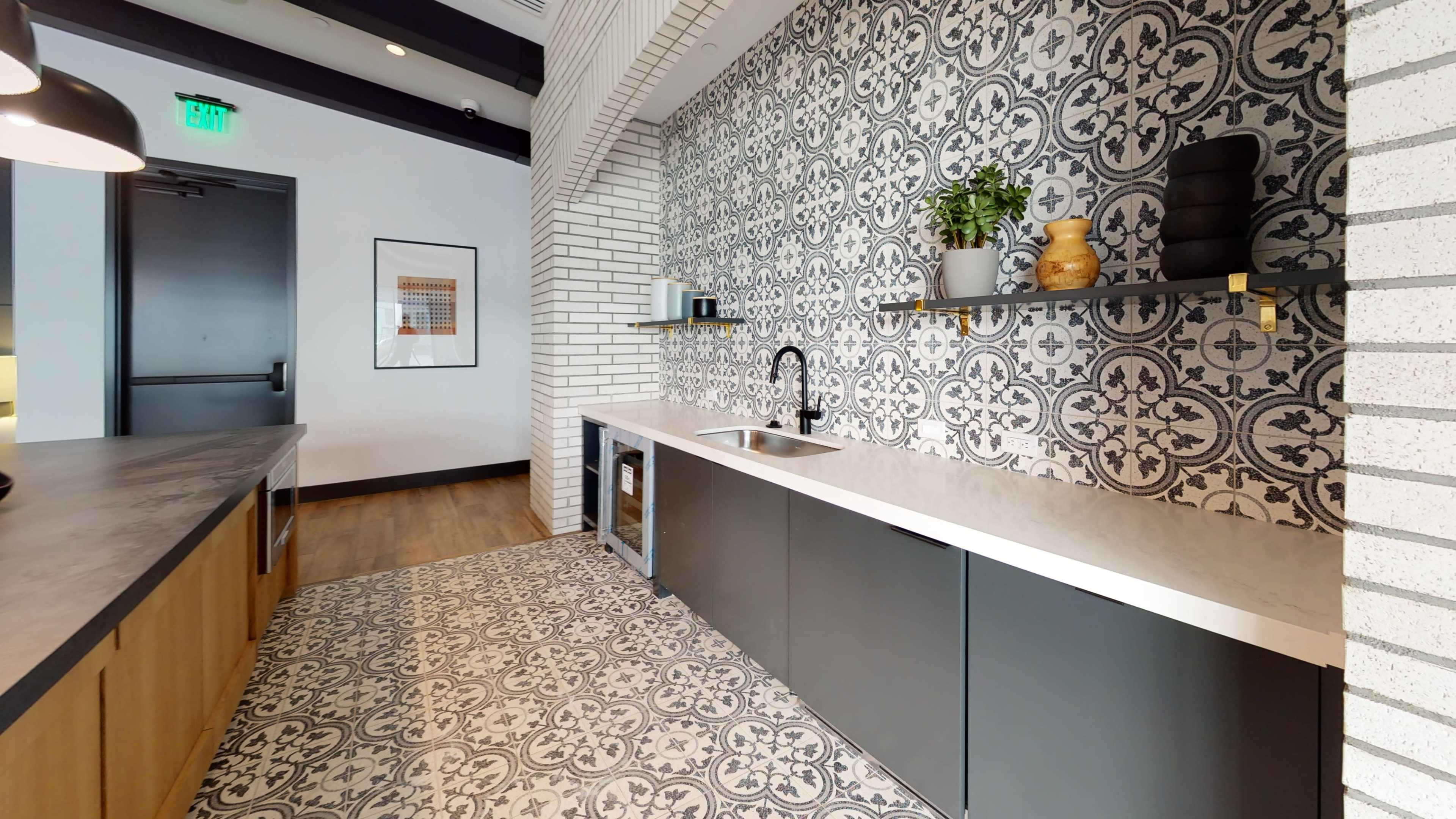 A modern kitchen featuring patterned tiles on the floor and backsplash, with a sink and shelving above a countertop.