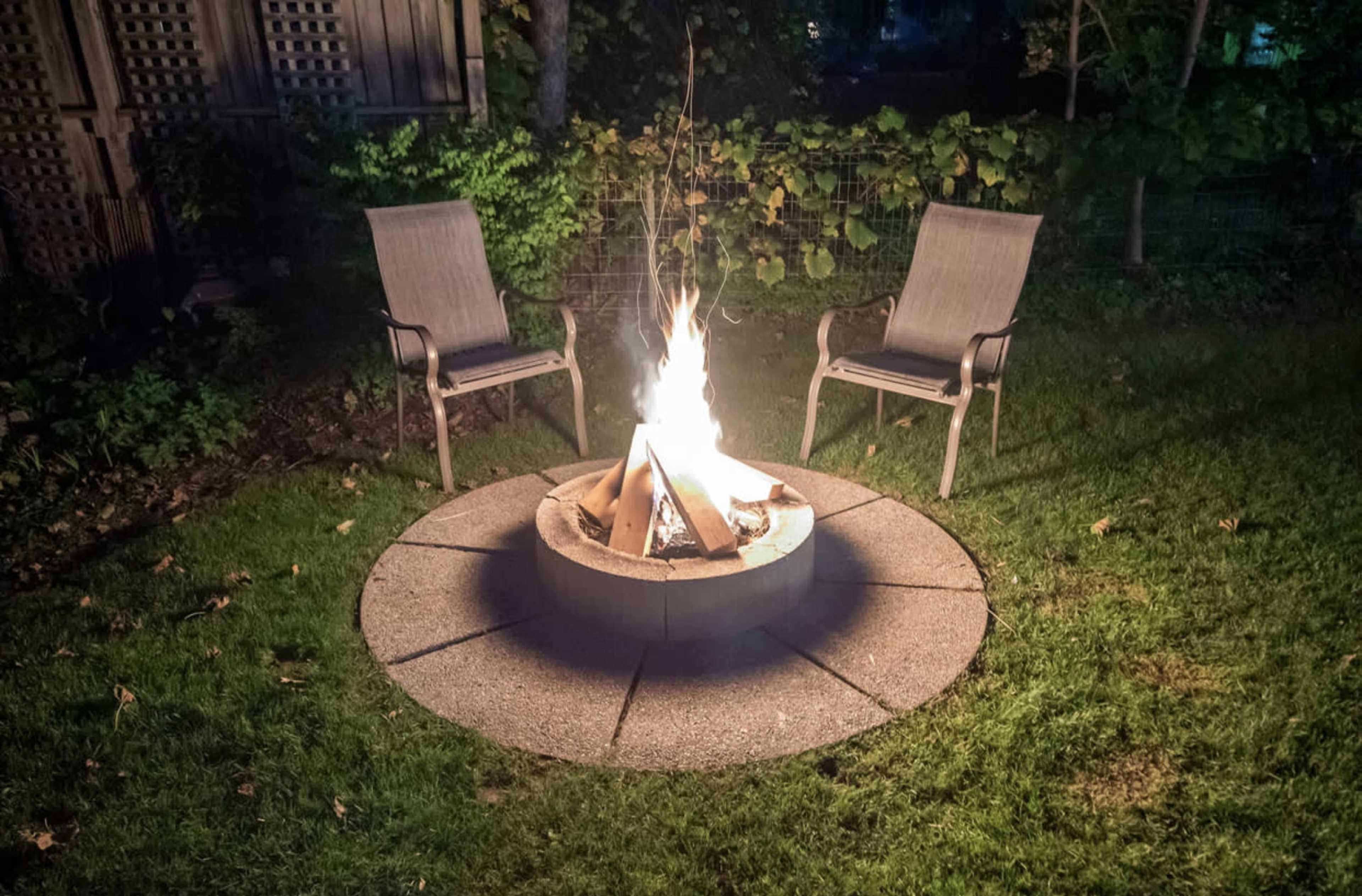 A fire pit surrounded by two chairs sits on a grassy area at night.