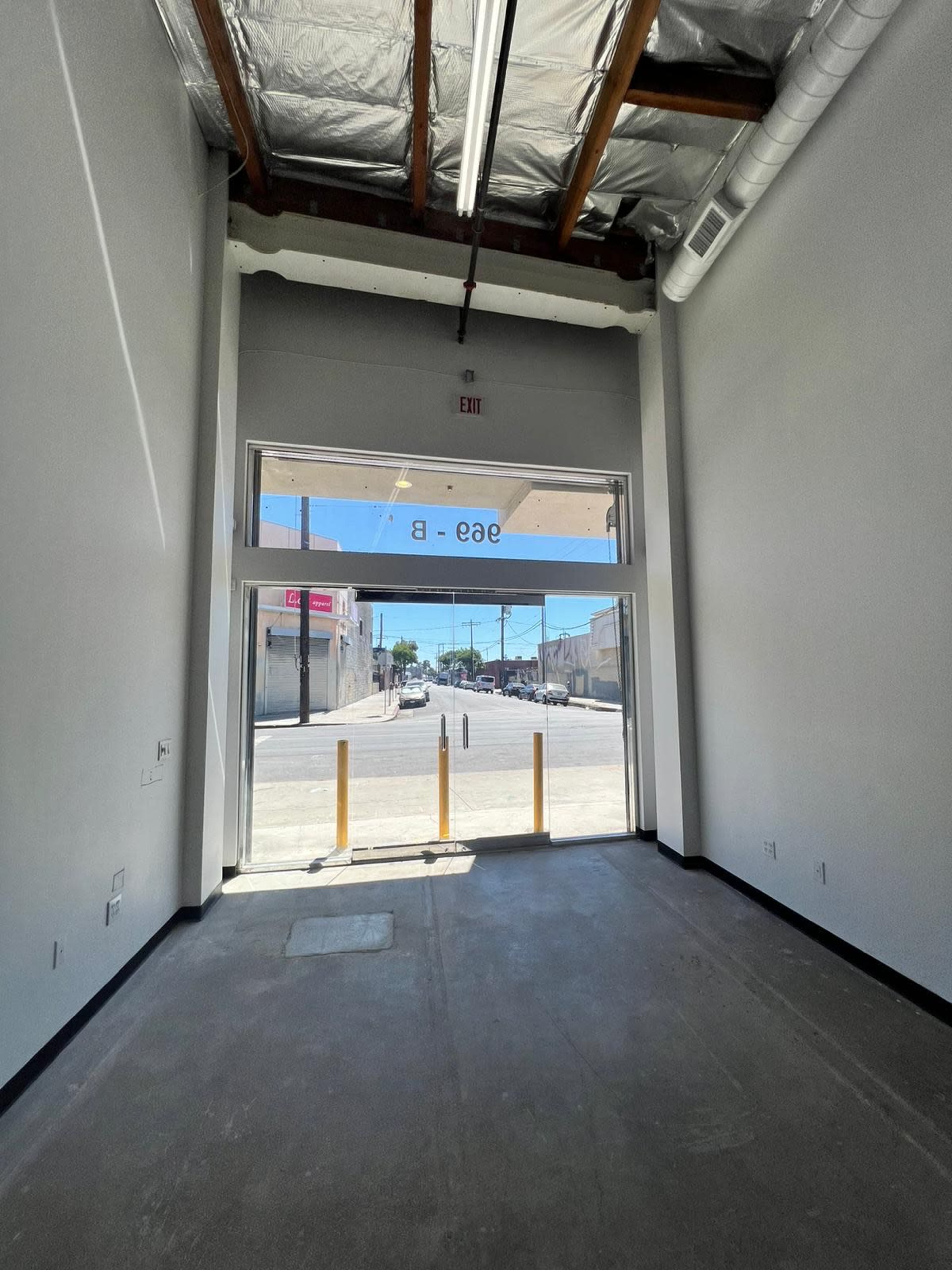The image shows an empty retail space with a large glass entrance facing a street, illuminated by natural light.