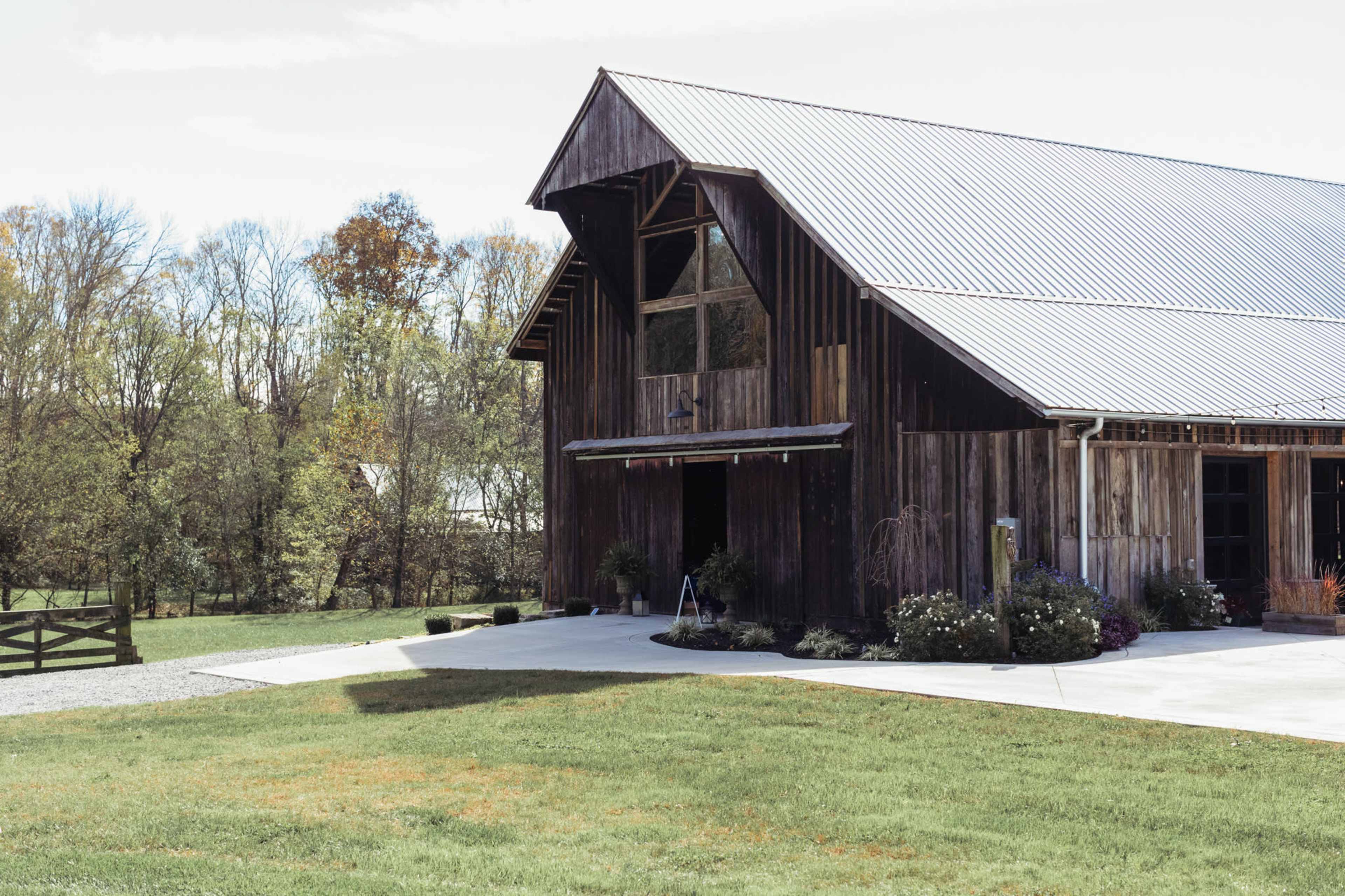 A large wooden barn with a metal roof is surrounded by green grass and trees in the background.