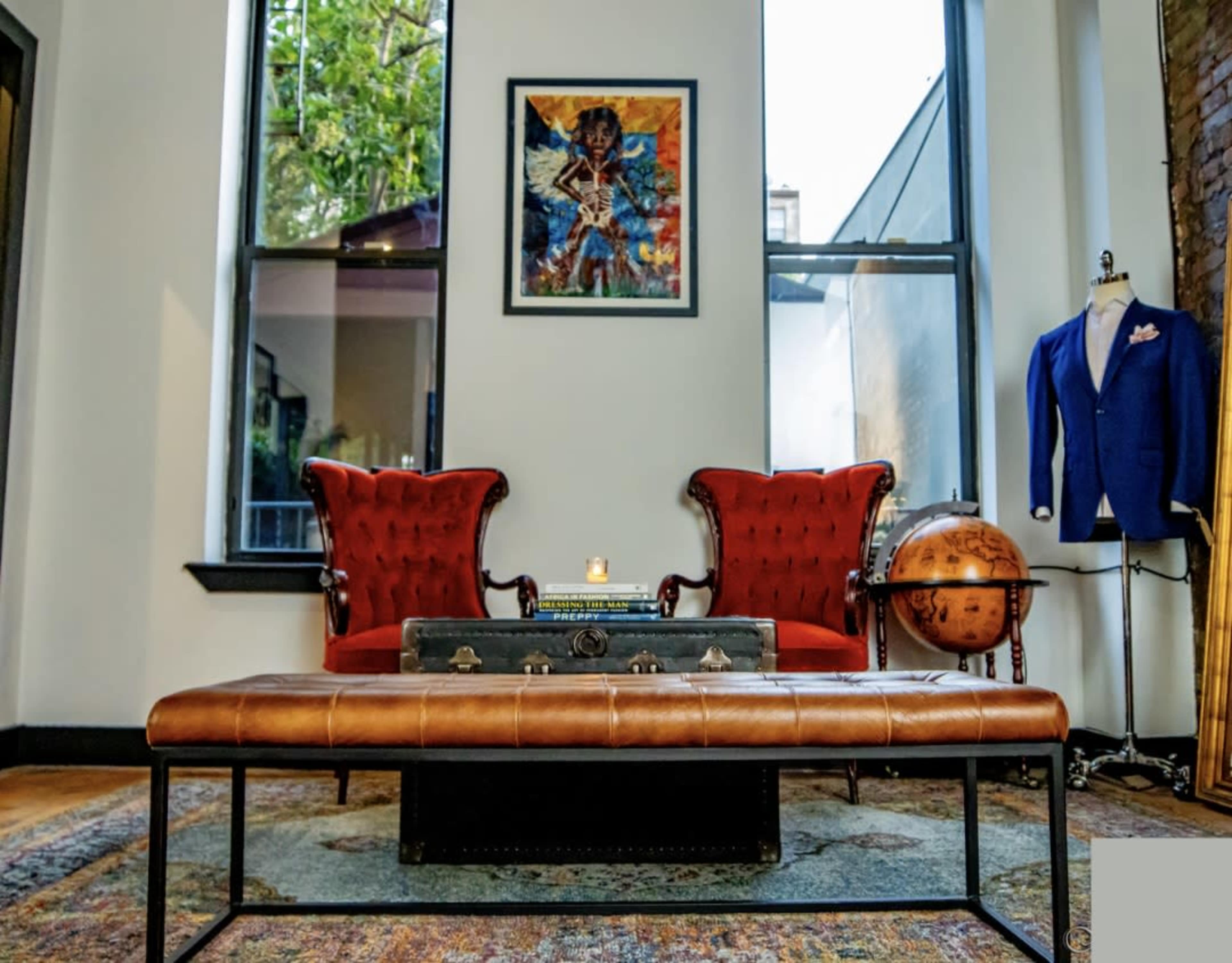 The image shows a stylish room featuring two red upholstered armchairs, a coffee table with a leather top, and a piece of artwork on the wall.