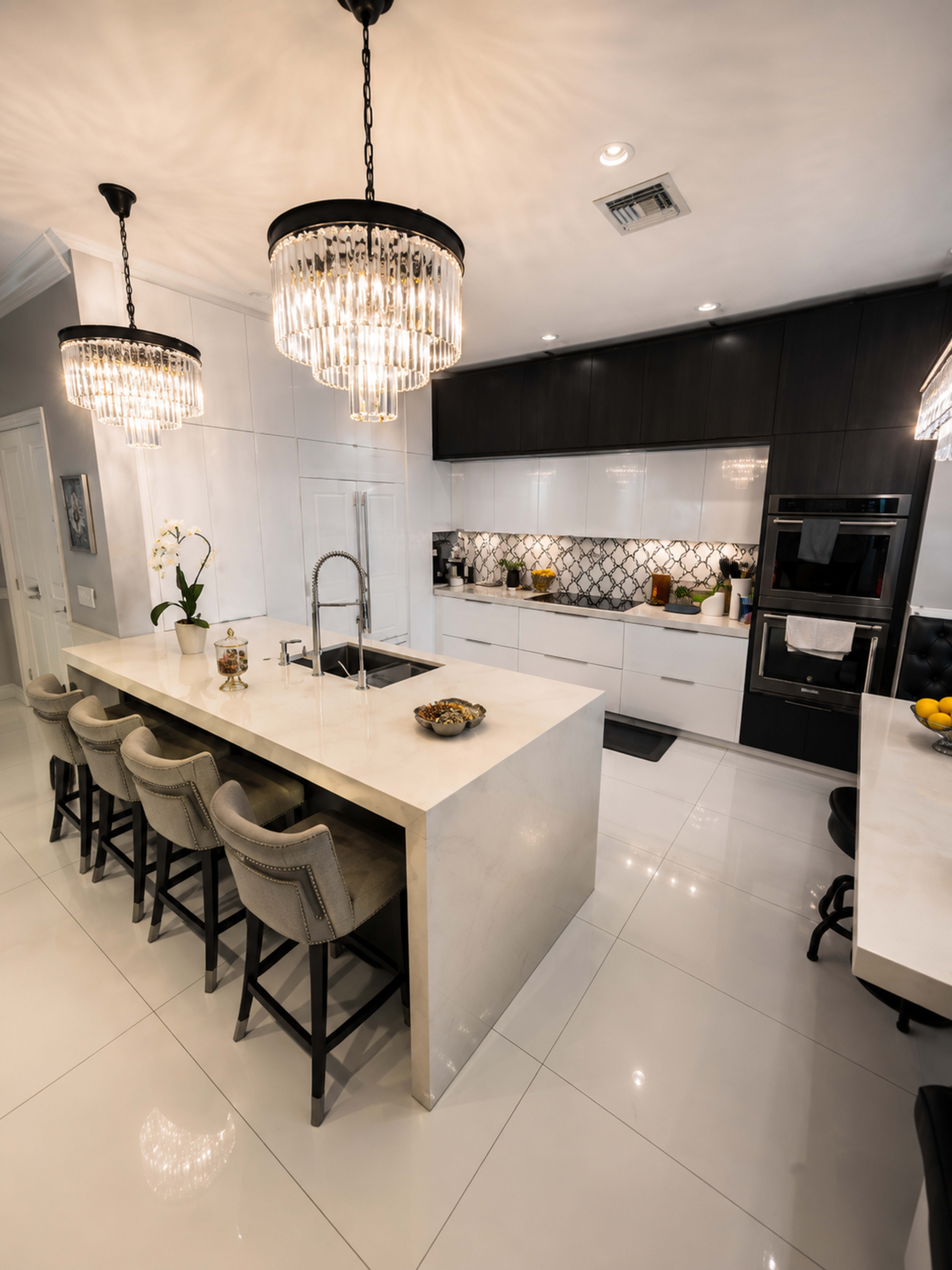 The image shows a modern kitchen featuring a large island with seating, sleek cabinetry, and stylish chandeliers.