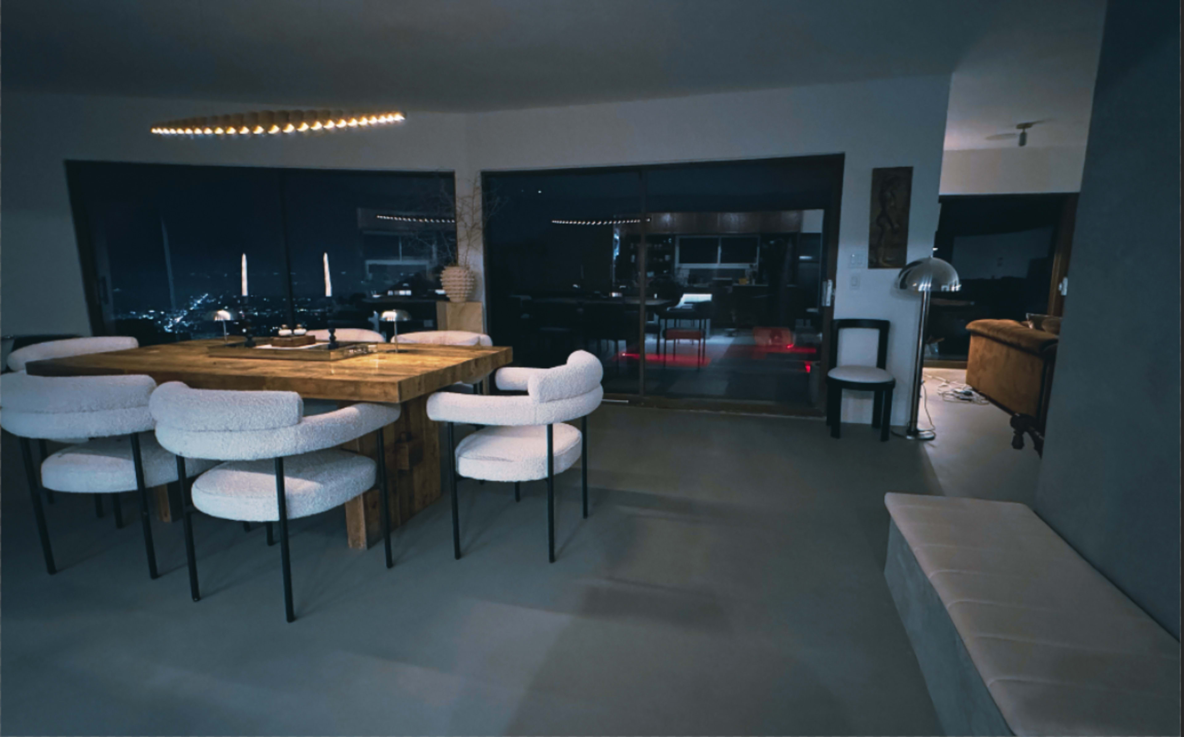 A spacious dining area features a large wooden table surrounded by upholstered chairs, with floor-to-ceiling windows offering a view of the city at night.