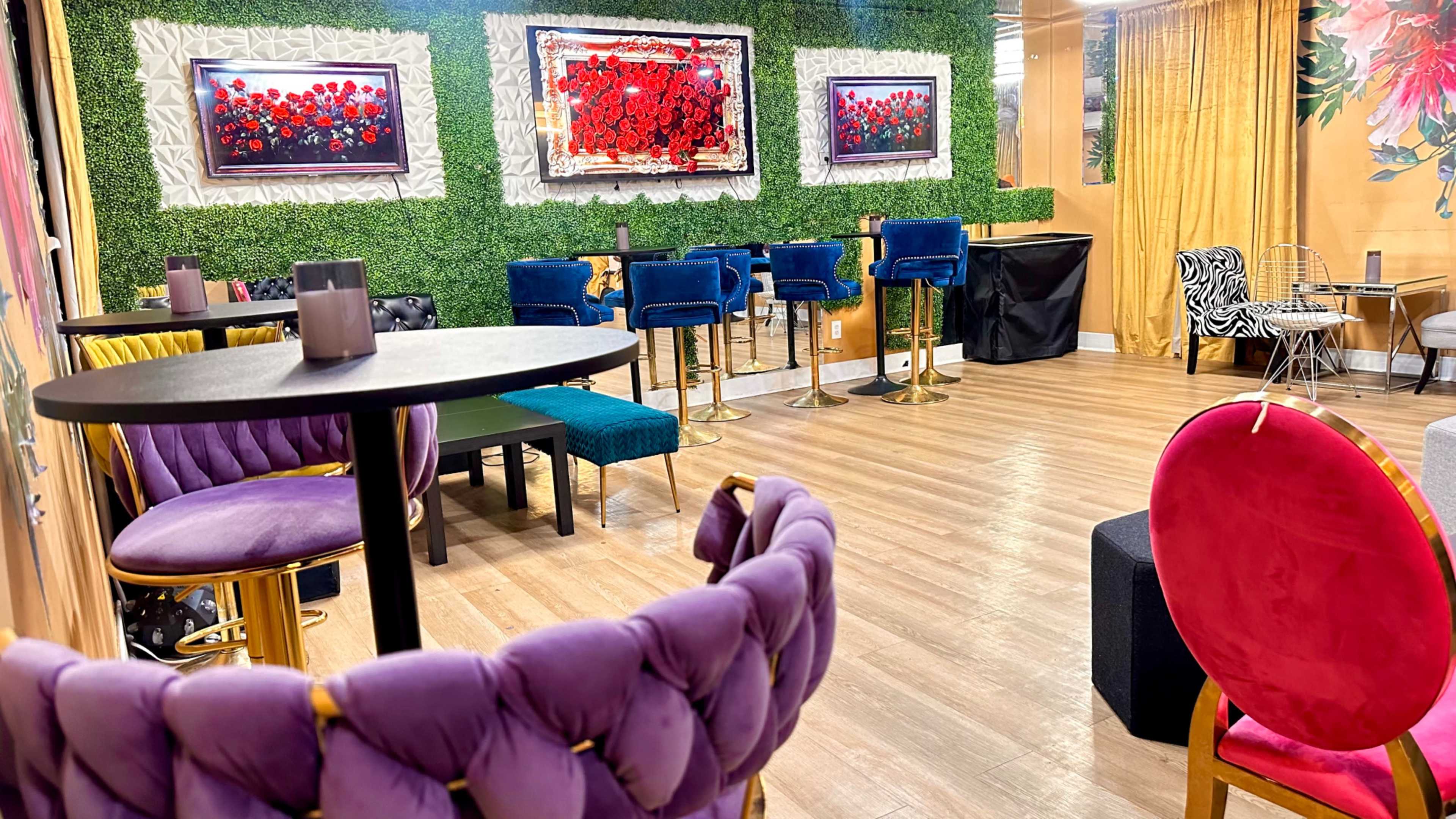 The image shows a modern lounge area featuring various seating options, including purple and blue chairs, and green wall decor with framed floral artwork.