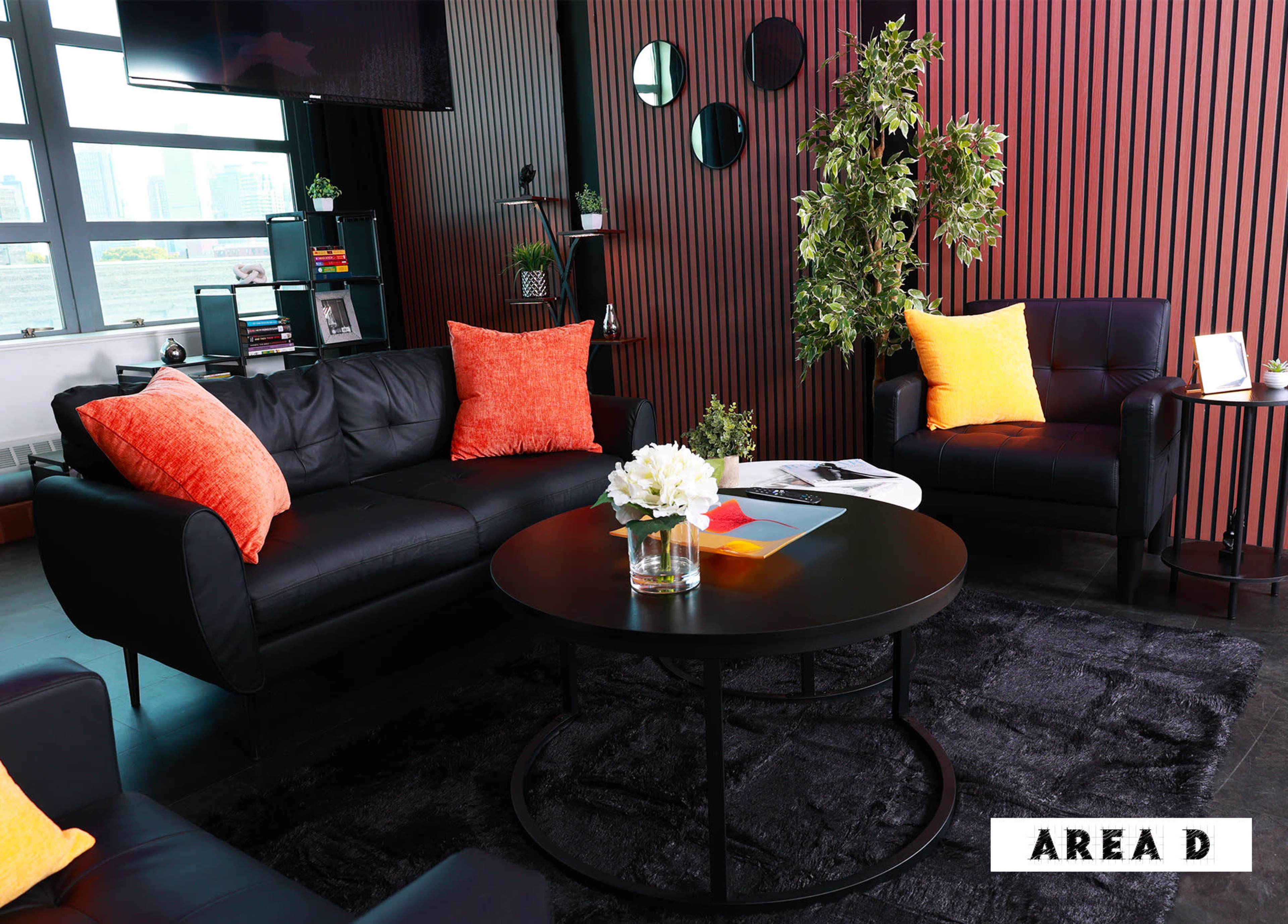 The image showcases a modern living room with a black leather sofa, two chairs, a round coffee table, and decorative plants against a backdrop of wooden paneling.