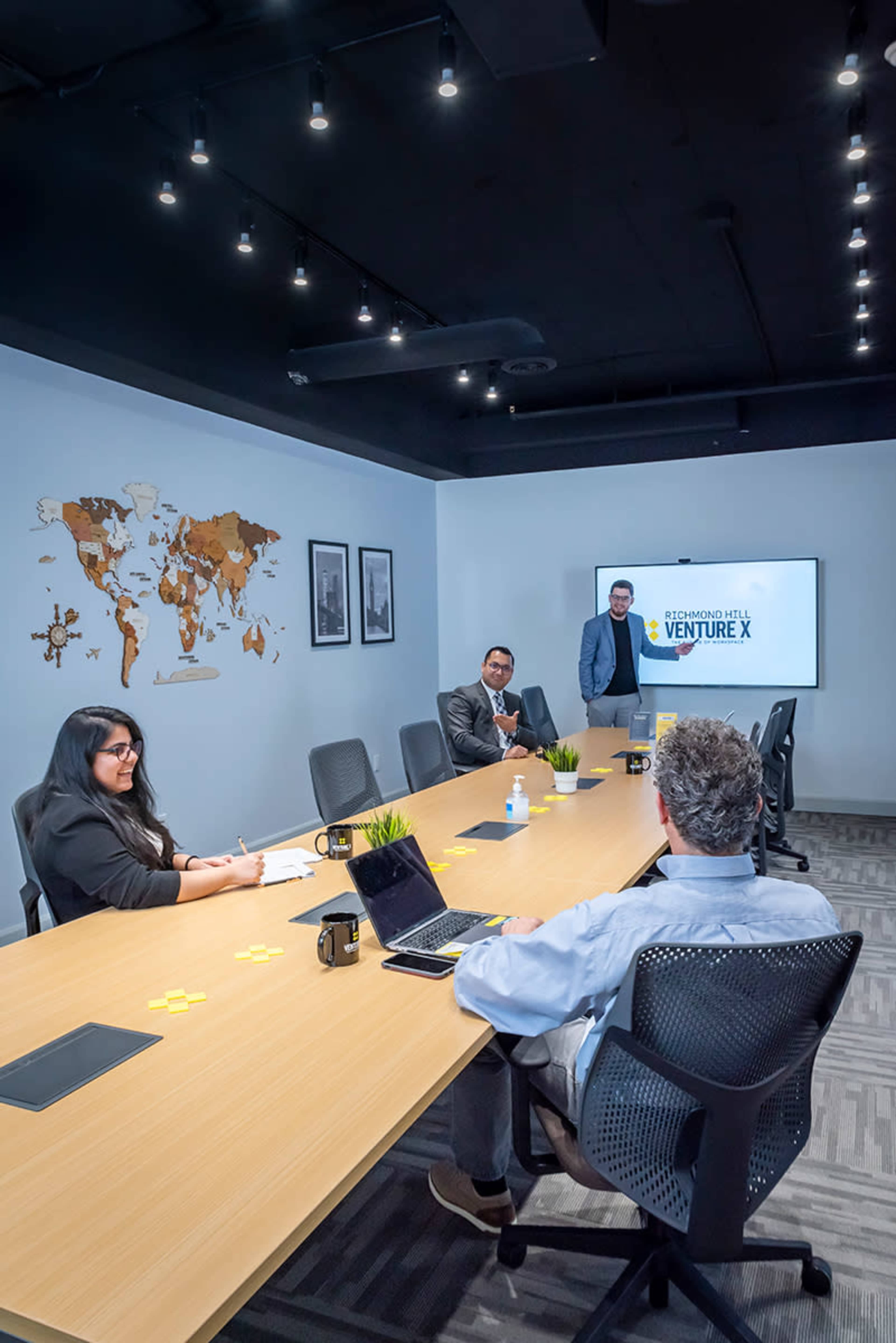 A business meeting is taking place in a modern conference room with a presentation on a screen and a world map on the wall.