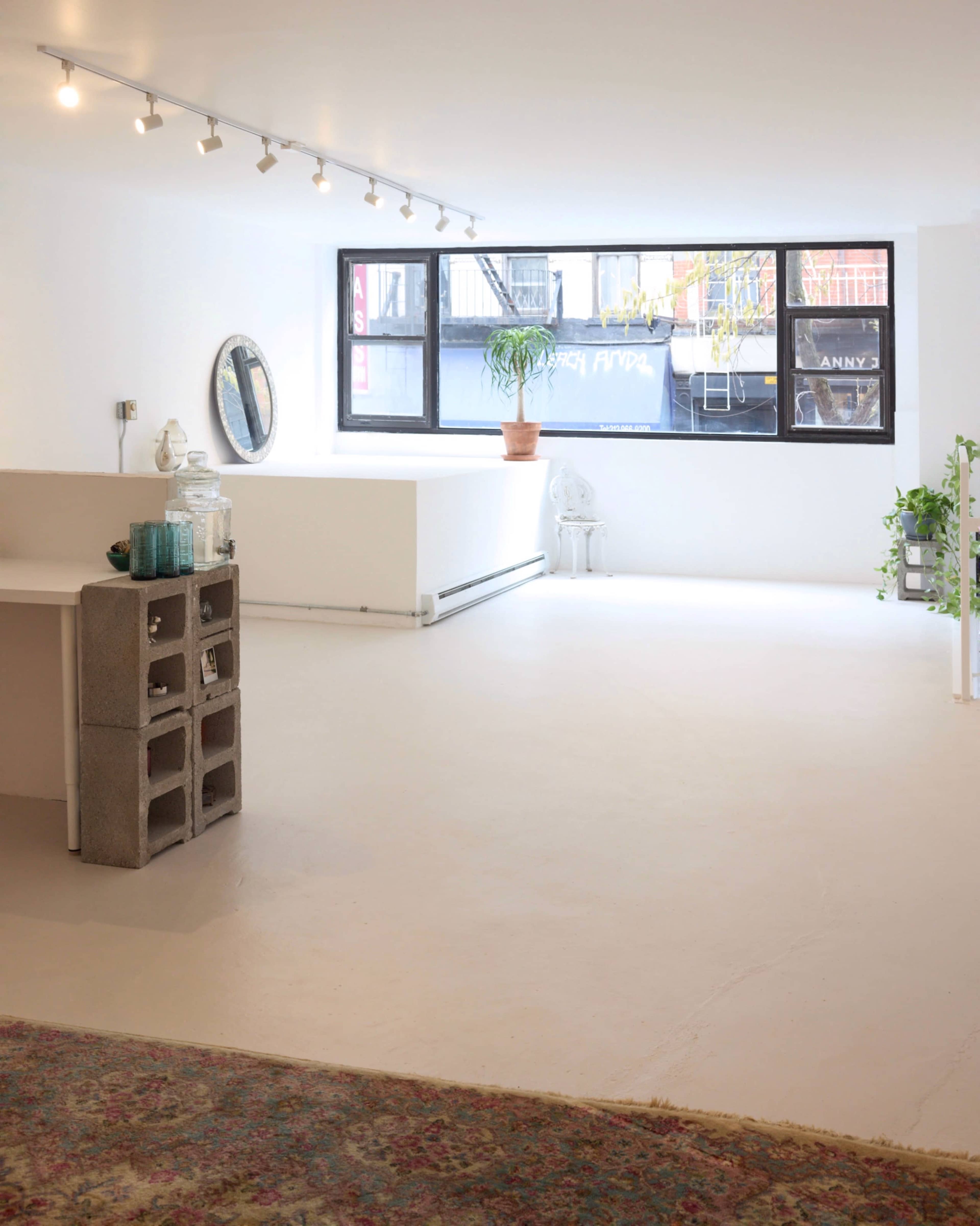 A bright, minimalist interior space with white walls, a concrete block shelf, a large window, and several plants.