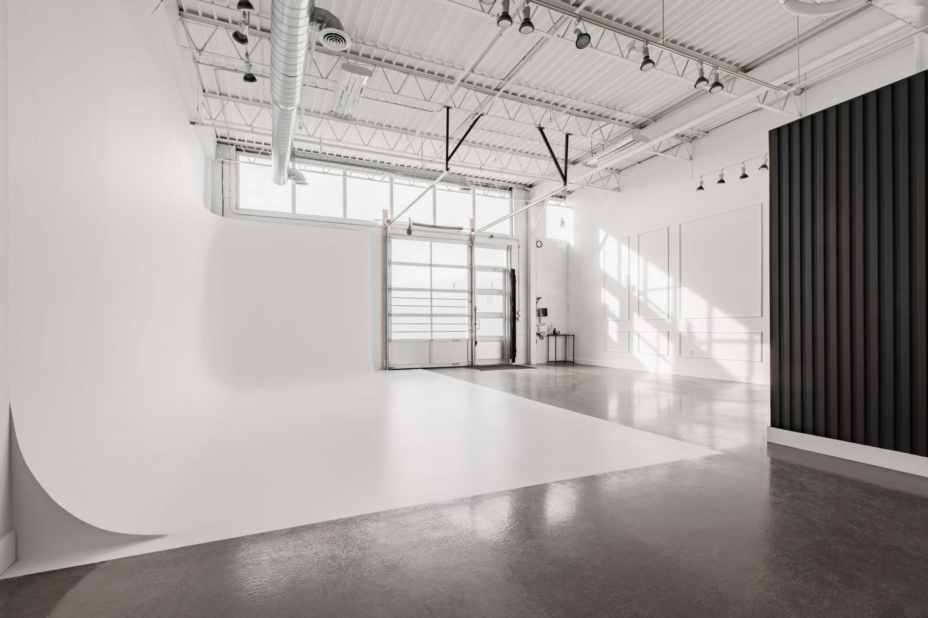 A spacious, well-lit studio with a white backdrop, polished concrete floor, and large windows.