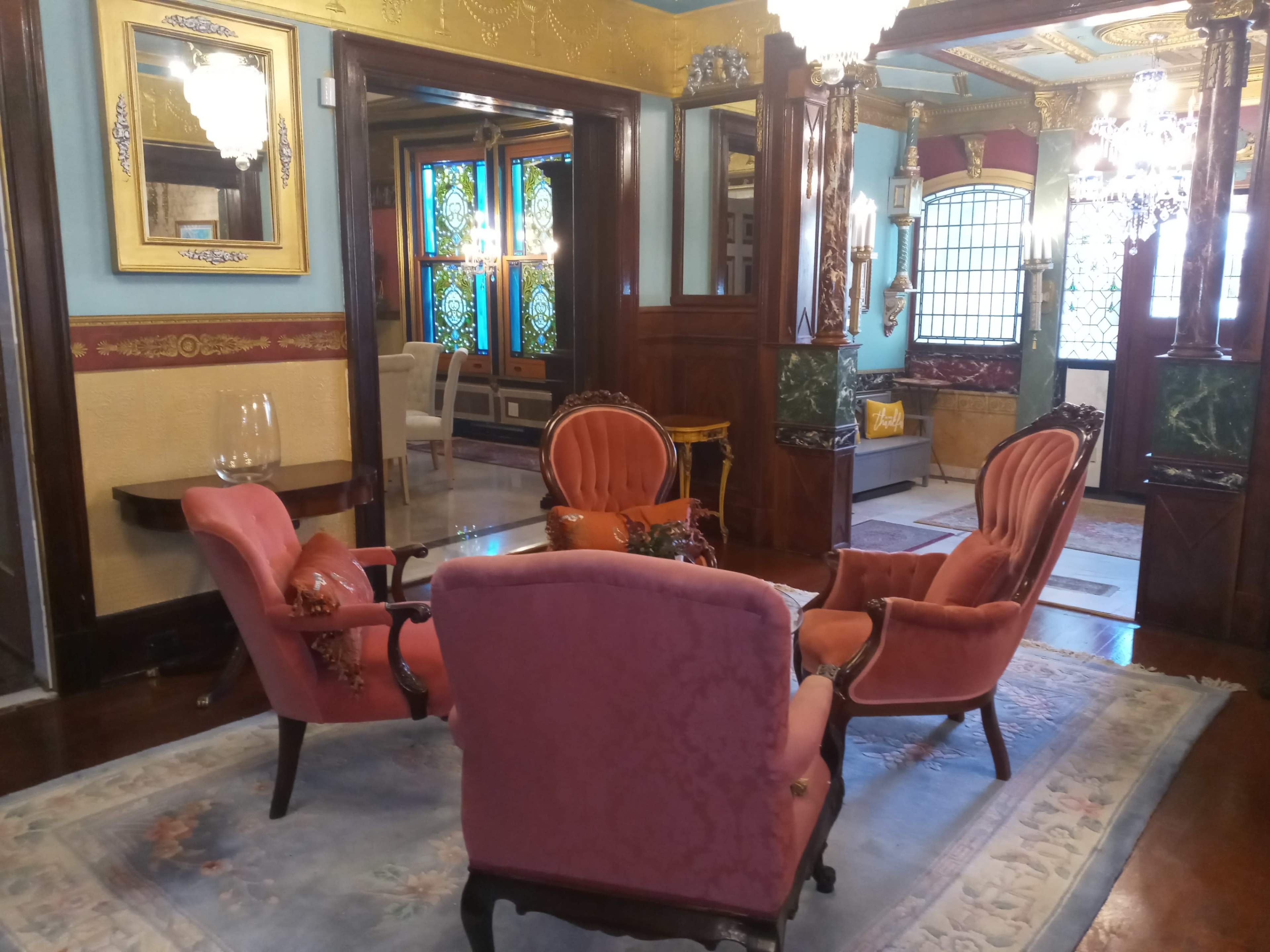 A vintage sitting area with four upholstered chairs arranged around a small table, surrounded by ornate decor and stained glass windows.