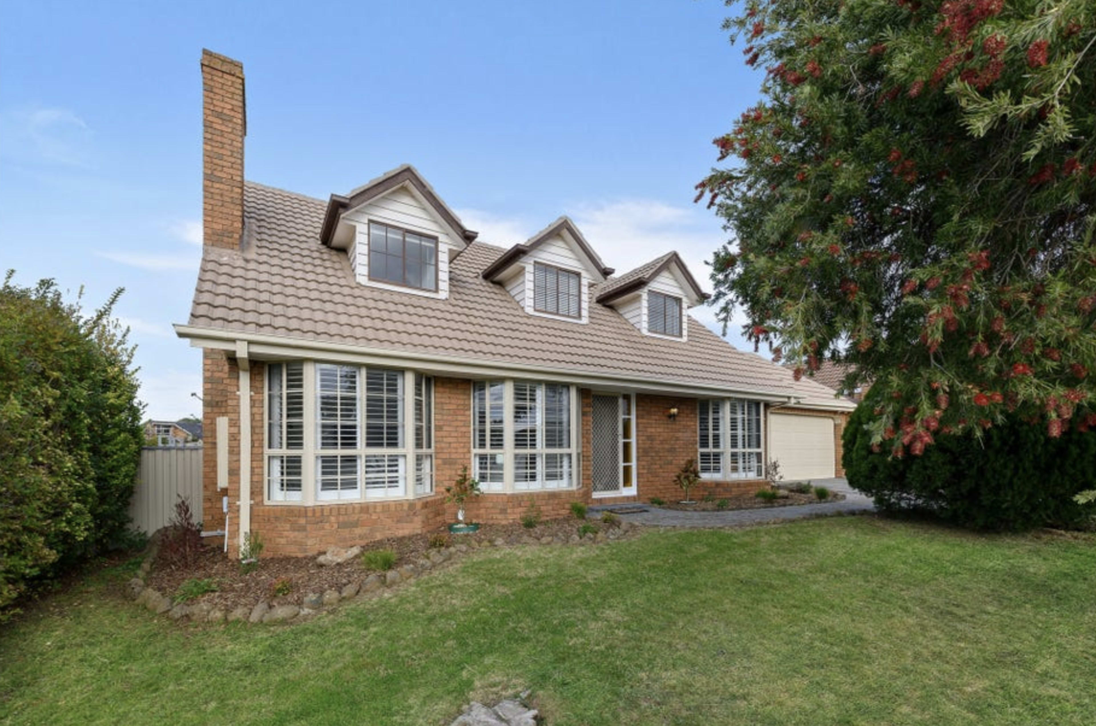 The image shows a two-story brick house with a gabled roof, surrounded by landscaped grass and shrubbery.