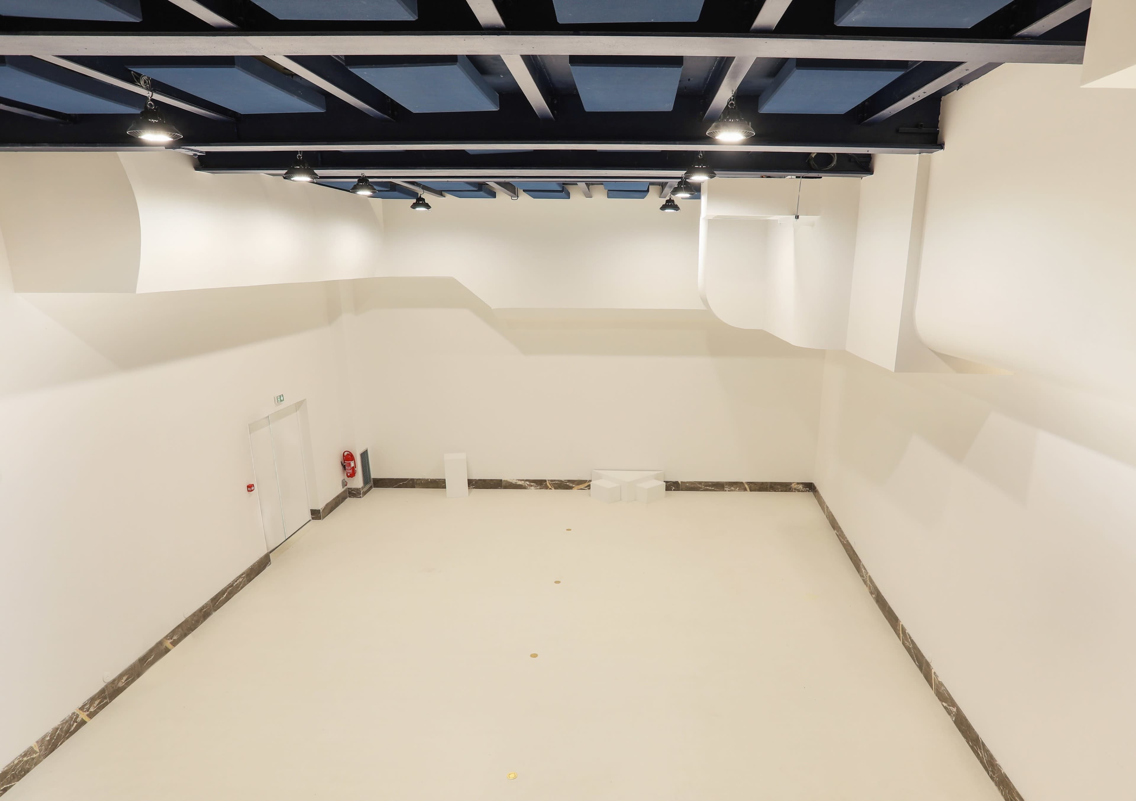 A spacious, empty room with white walls and a minimalistic design featuring a blue ceiling.