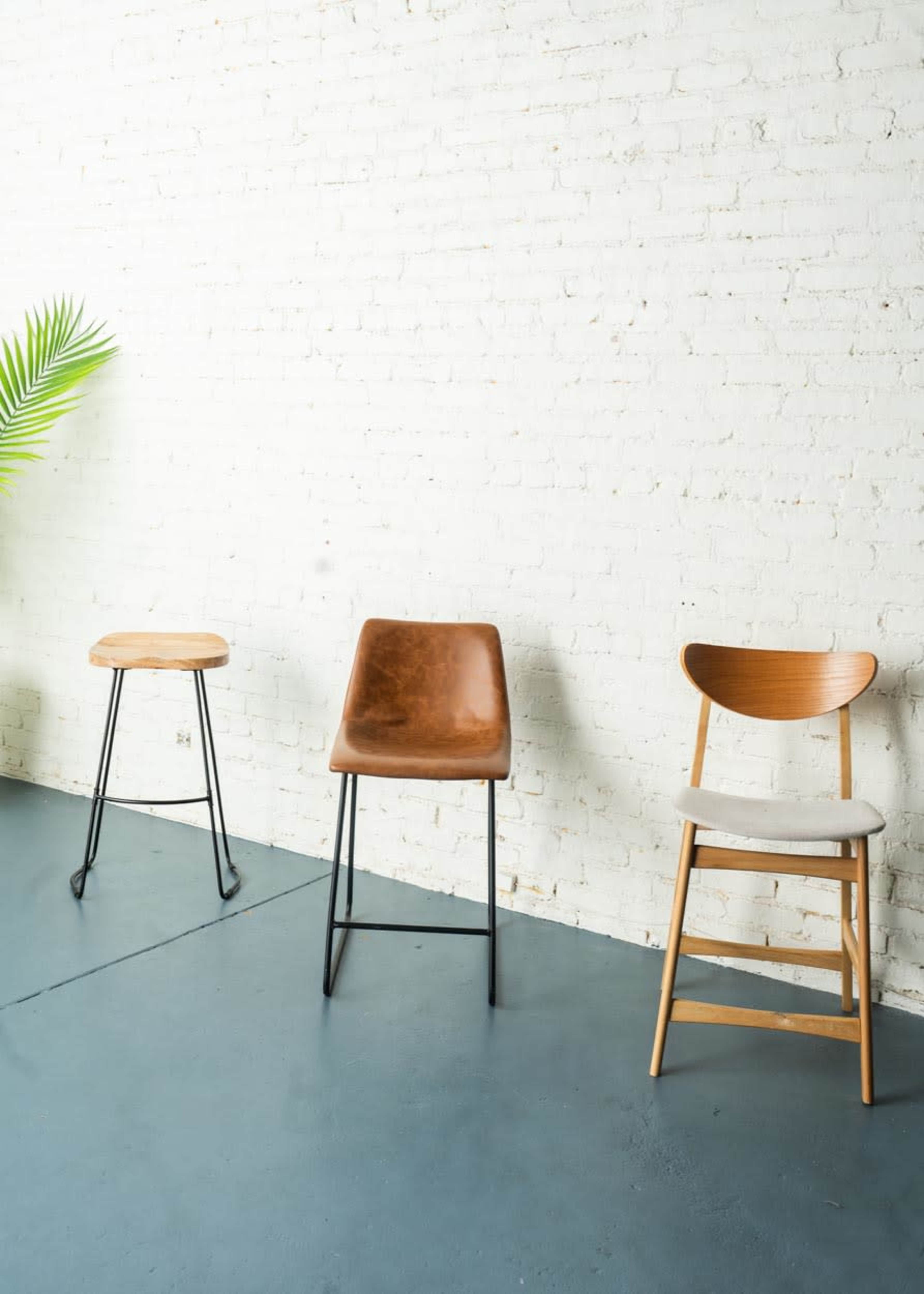 Three different styles of chairs arranged against a white brick wall, with a green plant in the background.
