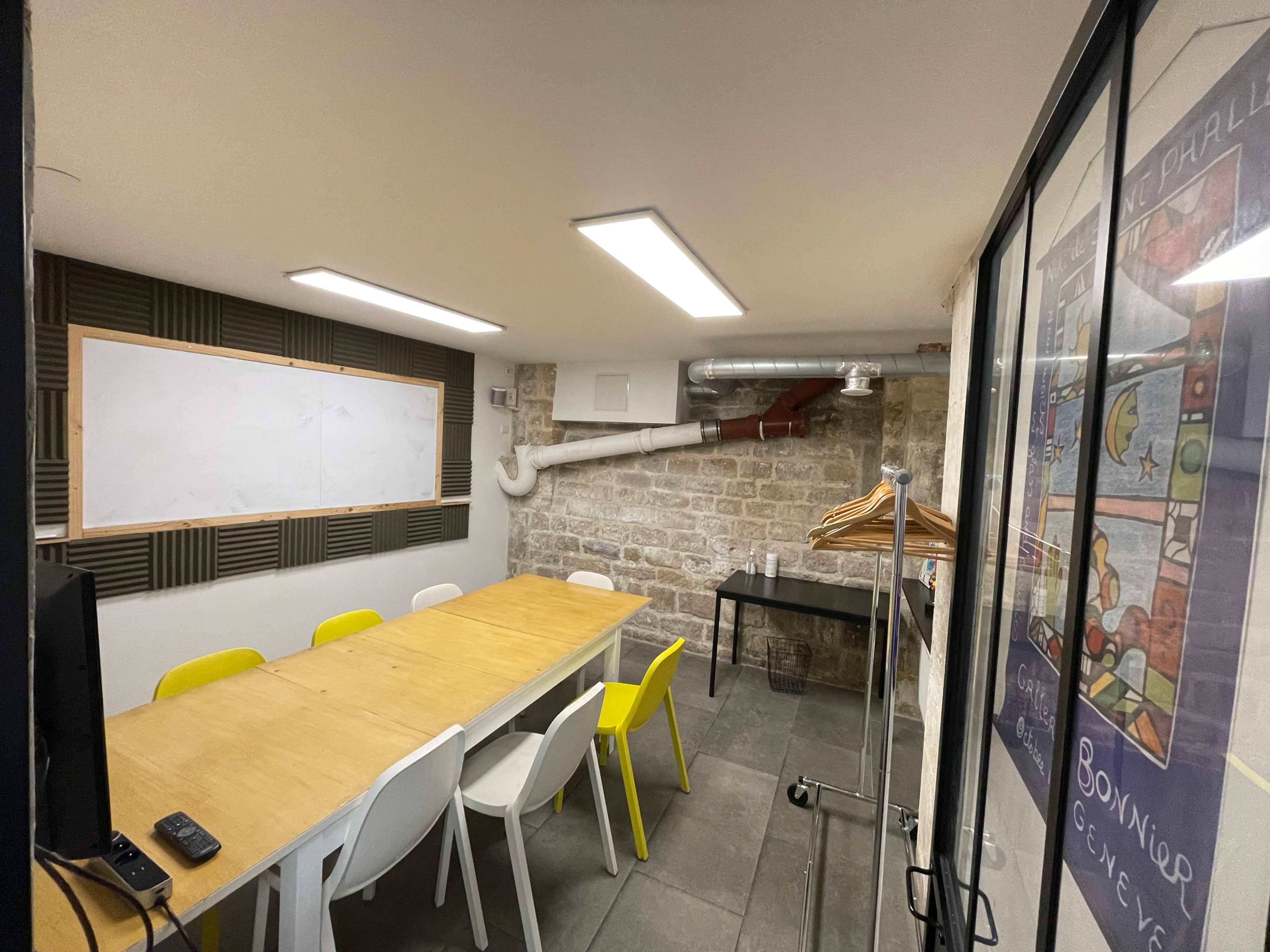 A small meeting room with a long wooden table surrounded by colorful chairs, a blank whiteboard, and exposed brick walls.