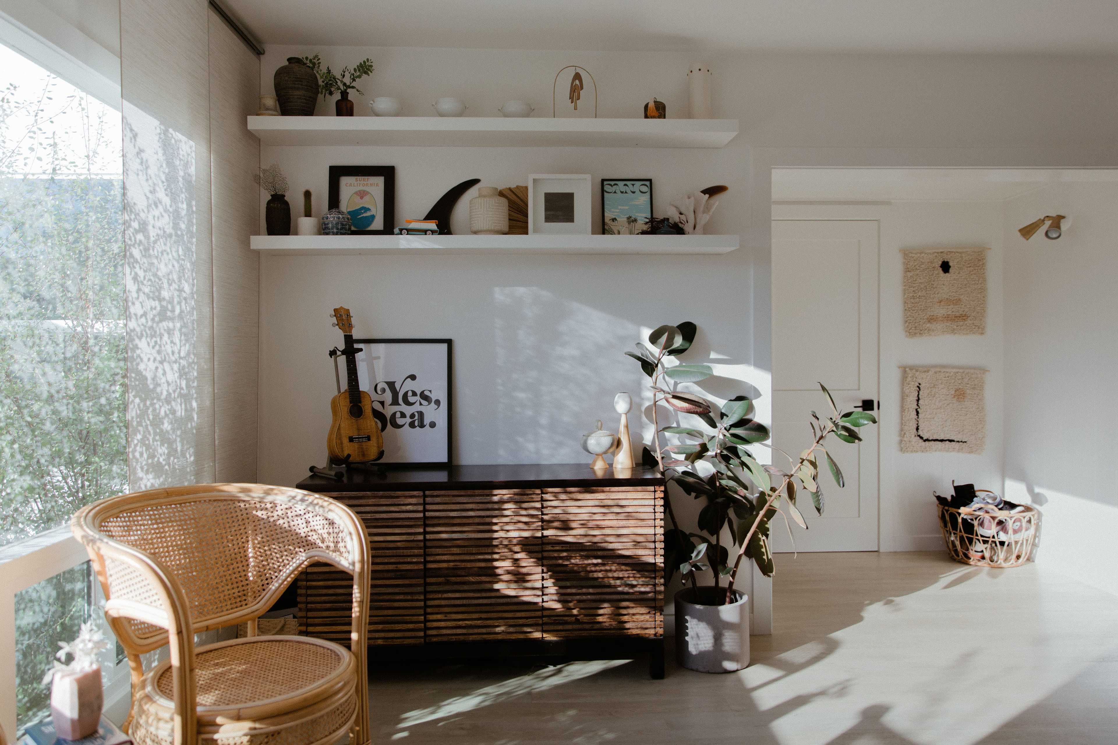 A bright room features a wooden sideboard adorned with decor items and a chair beside a window with natural light streaming in.