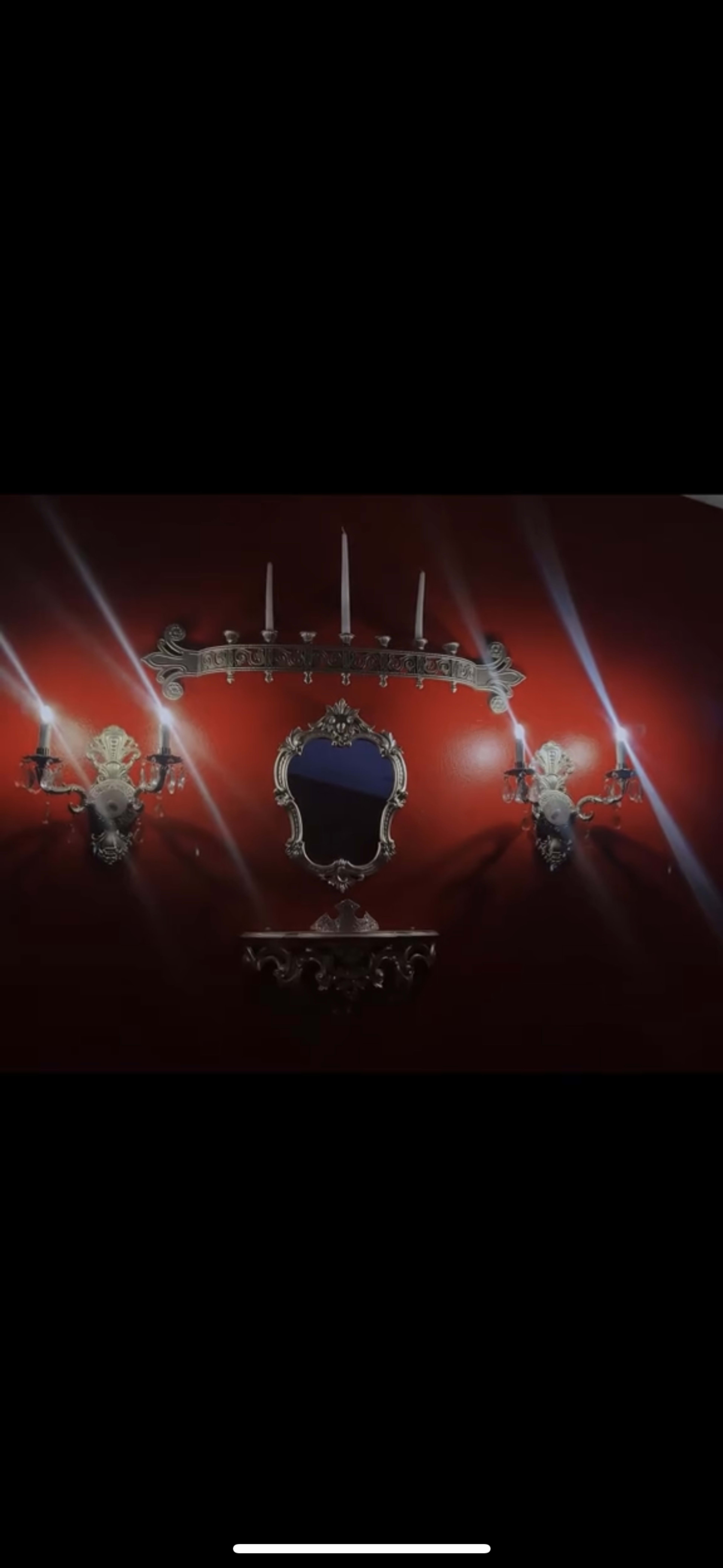 The image shows a red wall adorned with a decorative mirror and two ornate sconces, each holding a candle.
