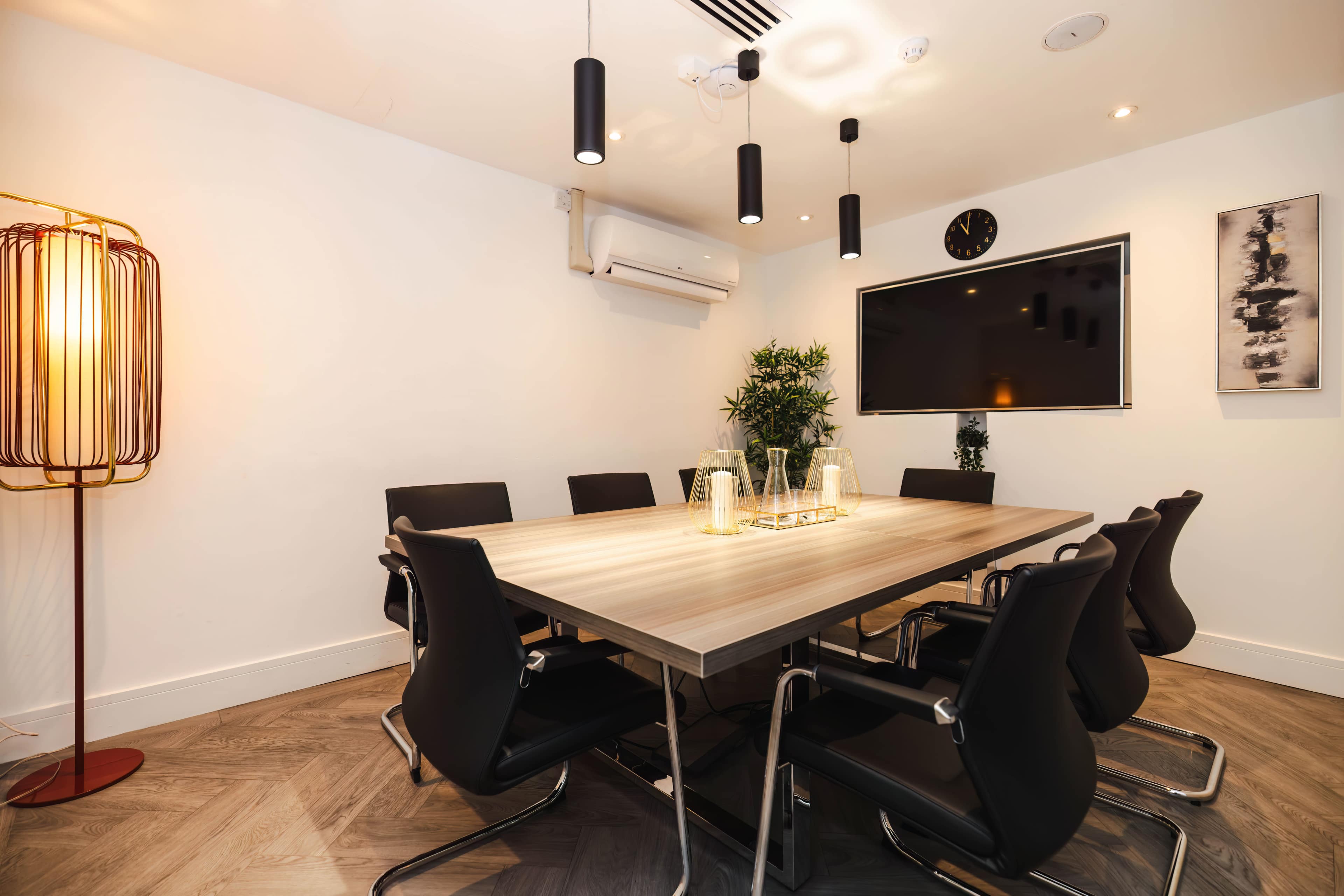 A modern conference room features a wooden table surrounded by black chairs, with ambient lighting and a wall-mounted screen.