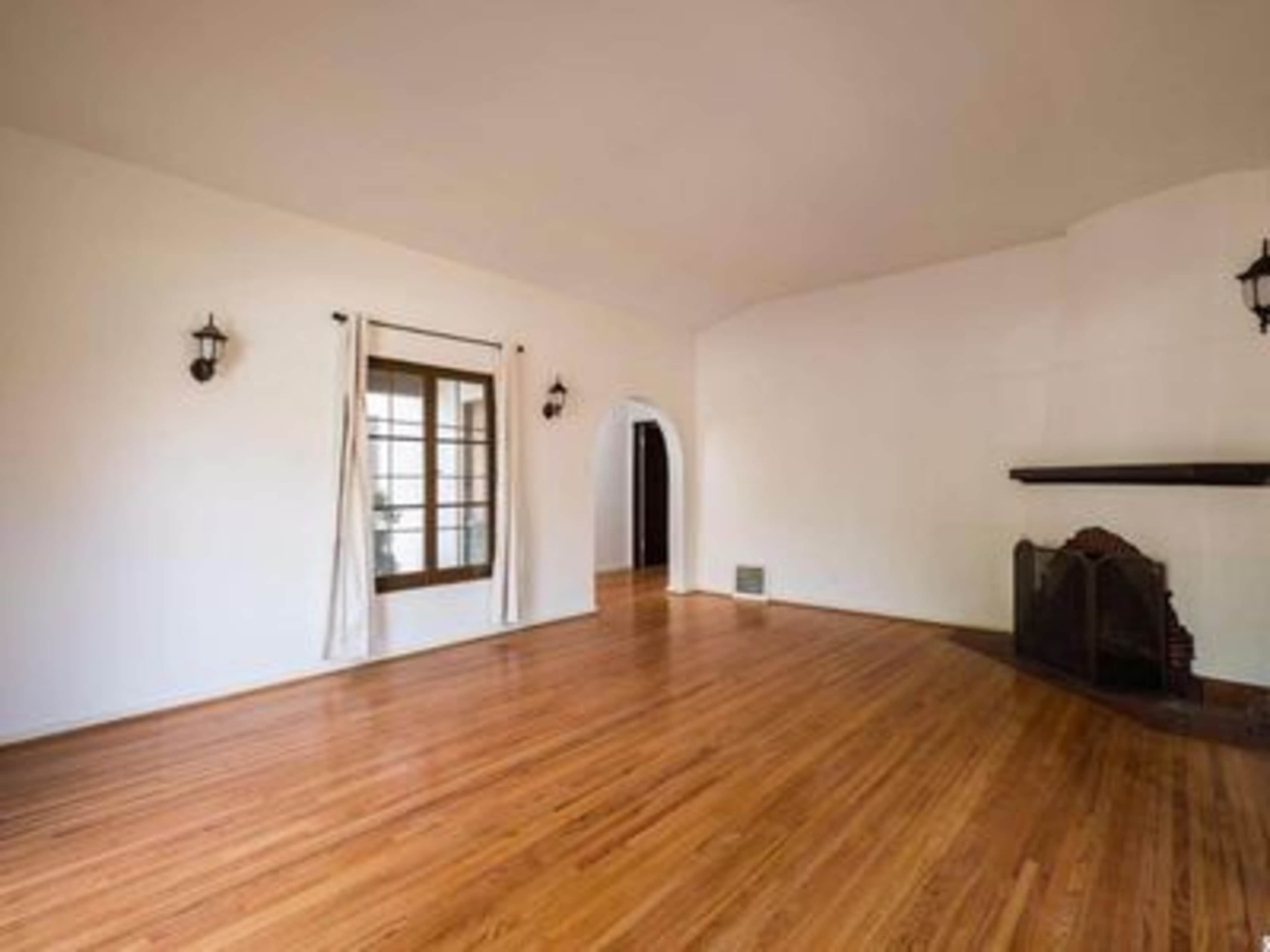 A spacious room with hardwood floors, white walls, and a fireplace against one wall.