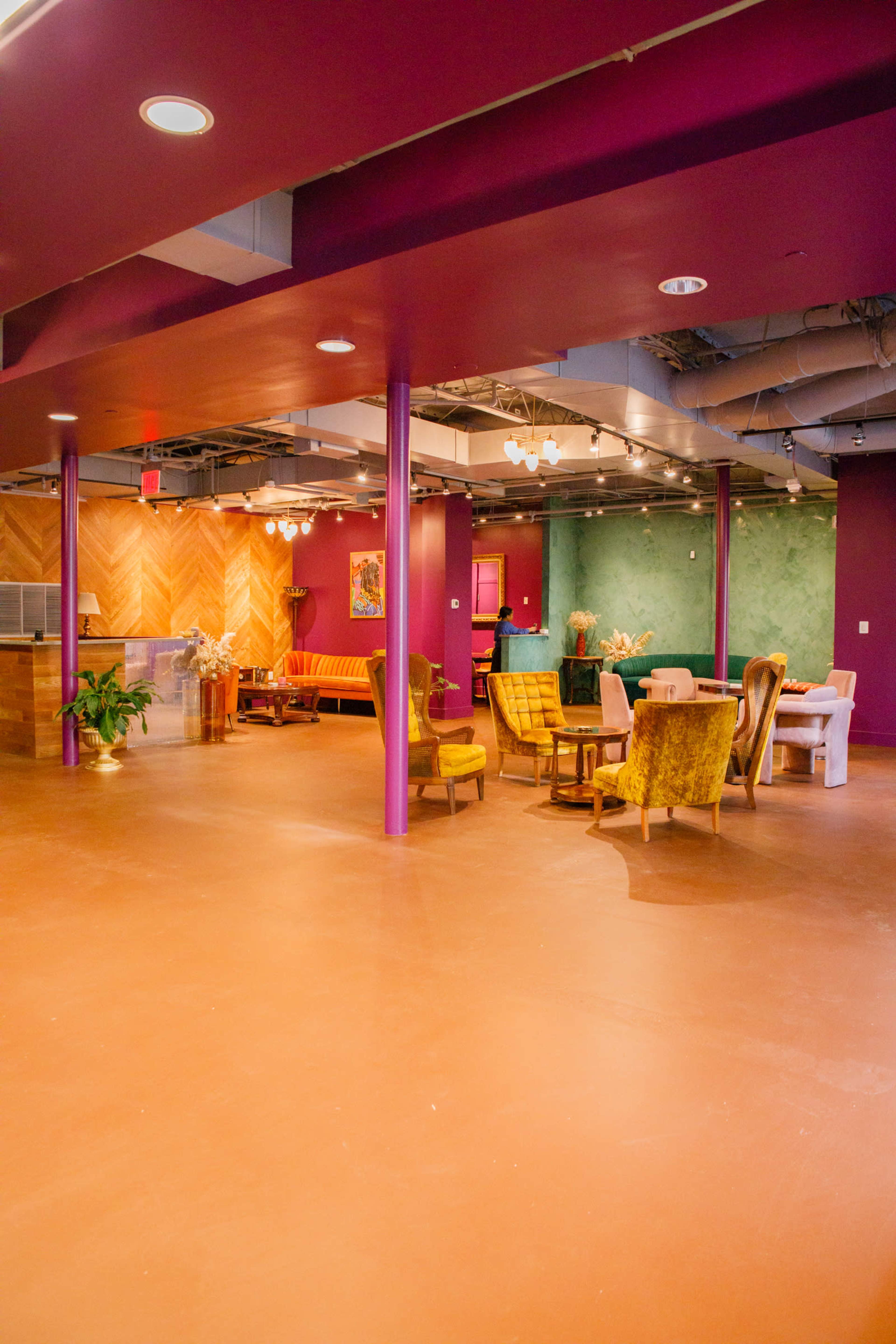 A spacious, brightly colored lounge area featuring various seating arrangements, including yellow chairs and a dining table, against a backdrop of deep purple and green walls.