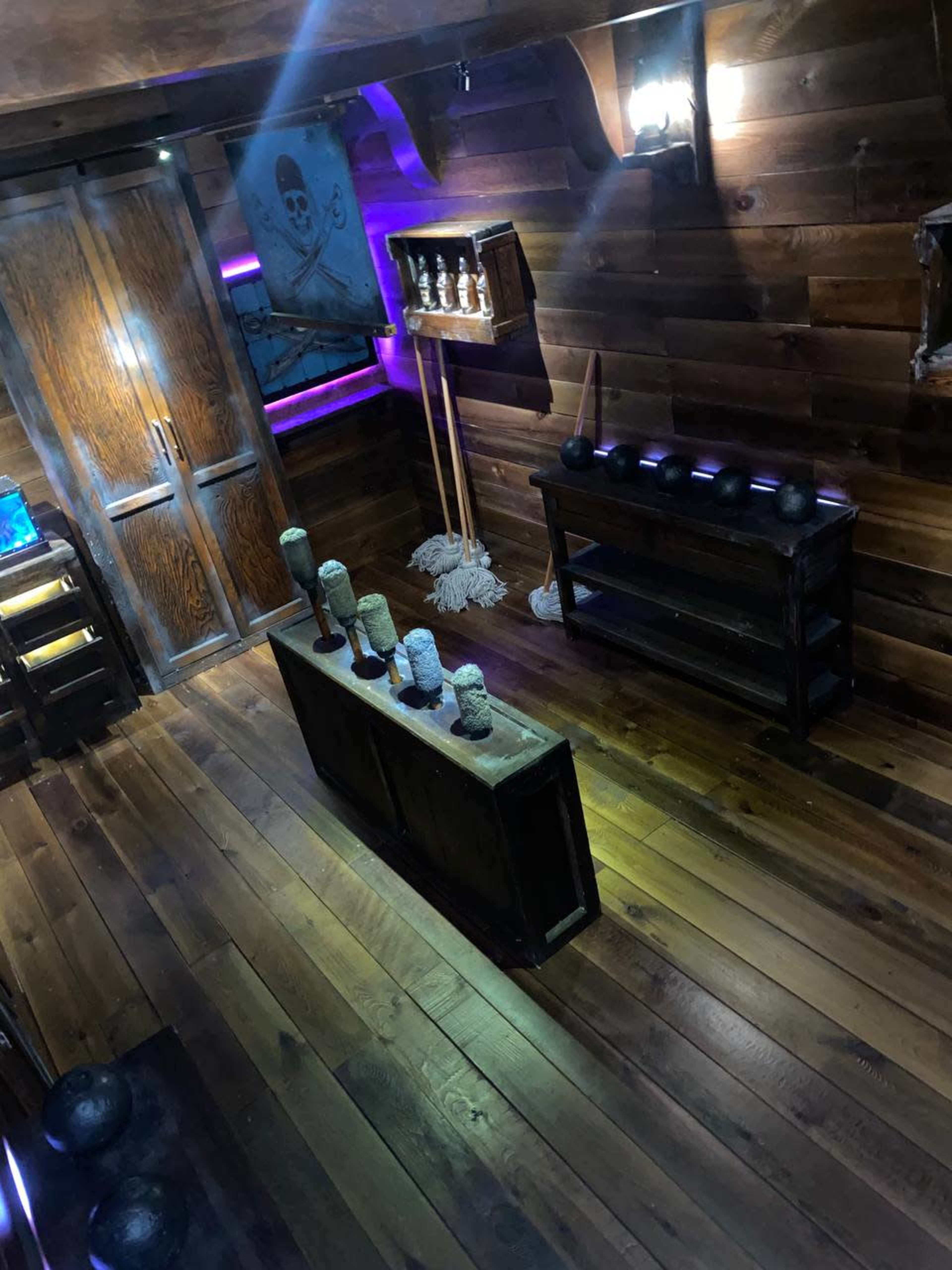 The image shows a dimly lit wooden room with pirate-themed decor, featuring a row of small barrels and a wooden cabinet against the wall.