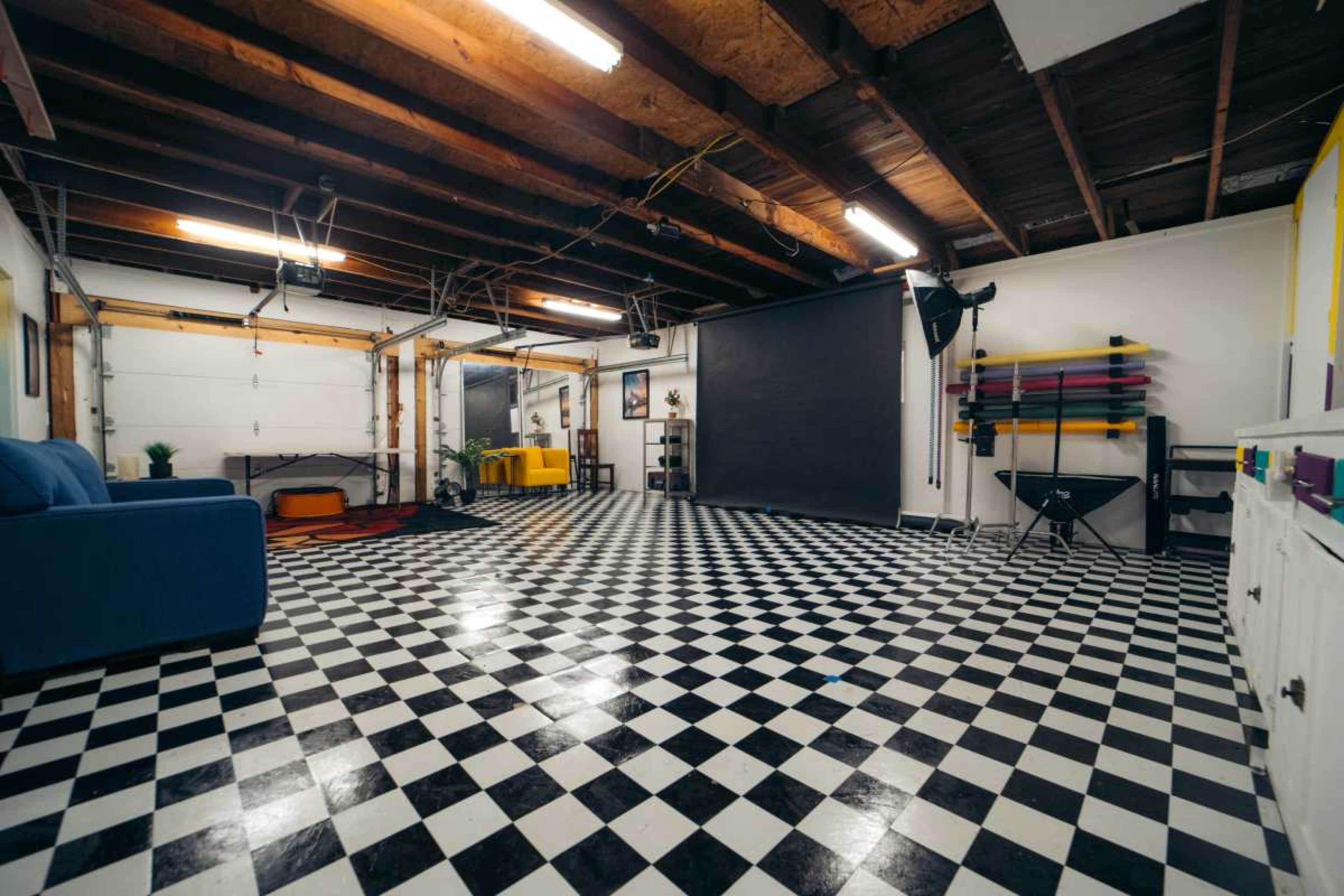 A spacious room with a black and white checkered floor, a blue couch, and various furnishings against the walls.