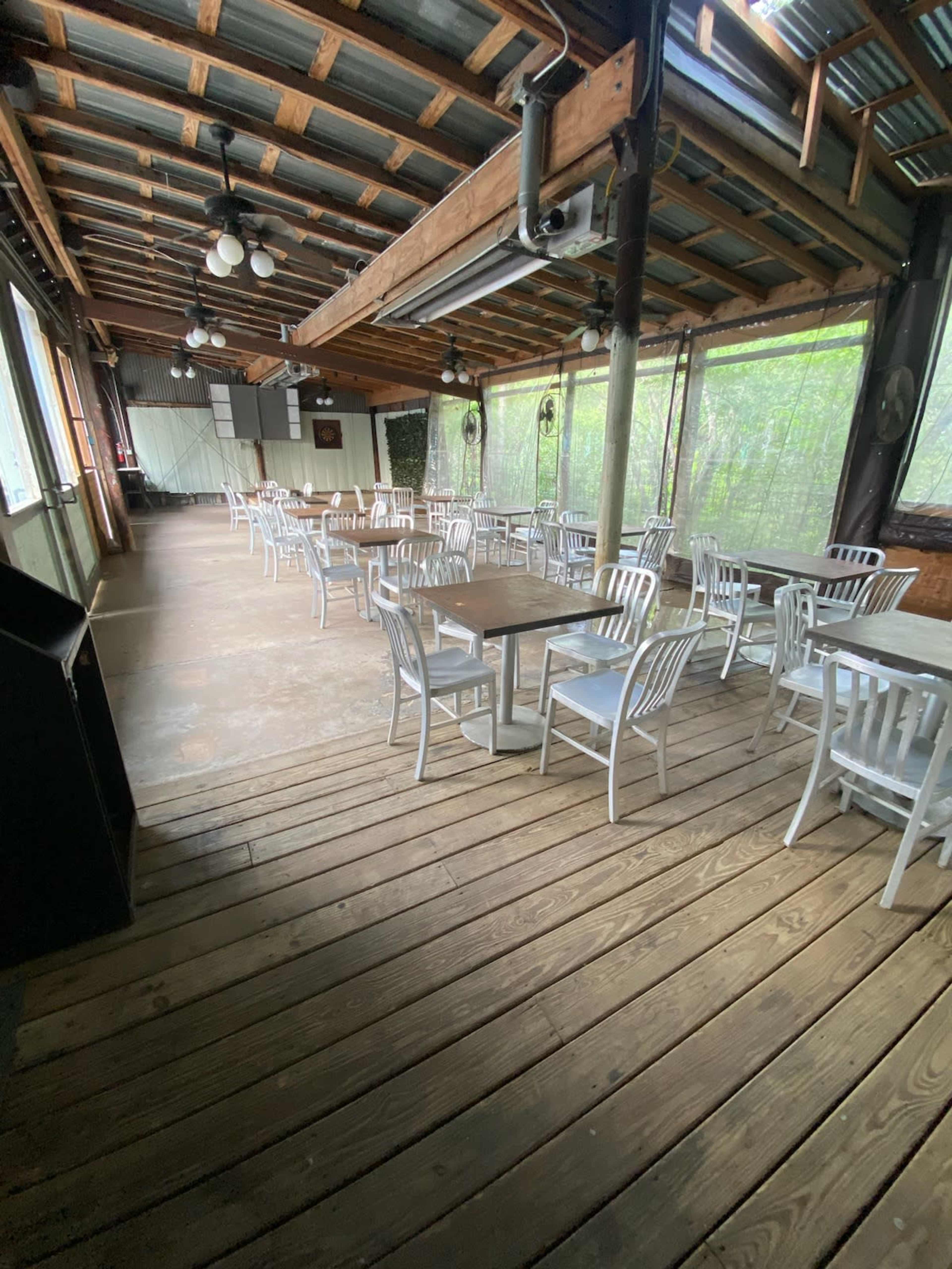 A spacious, empty dining area with wooden flooring and metal chairs arranged around small tables.