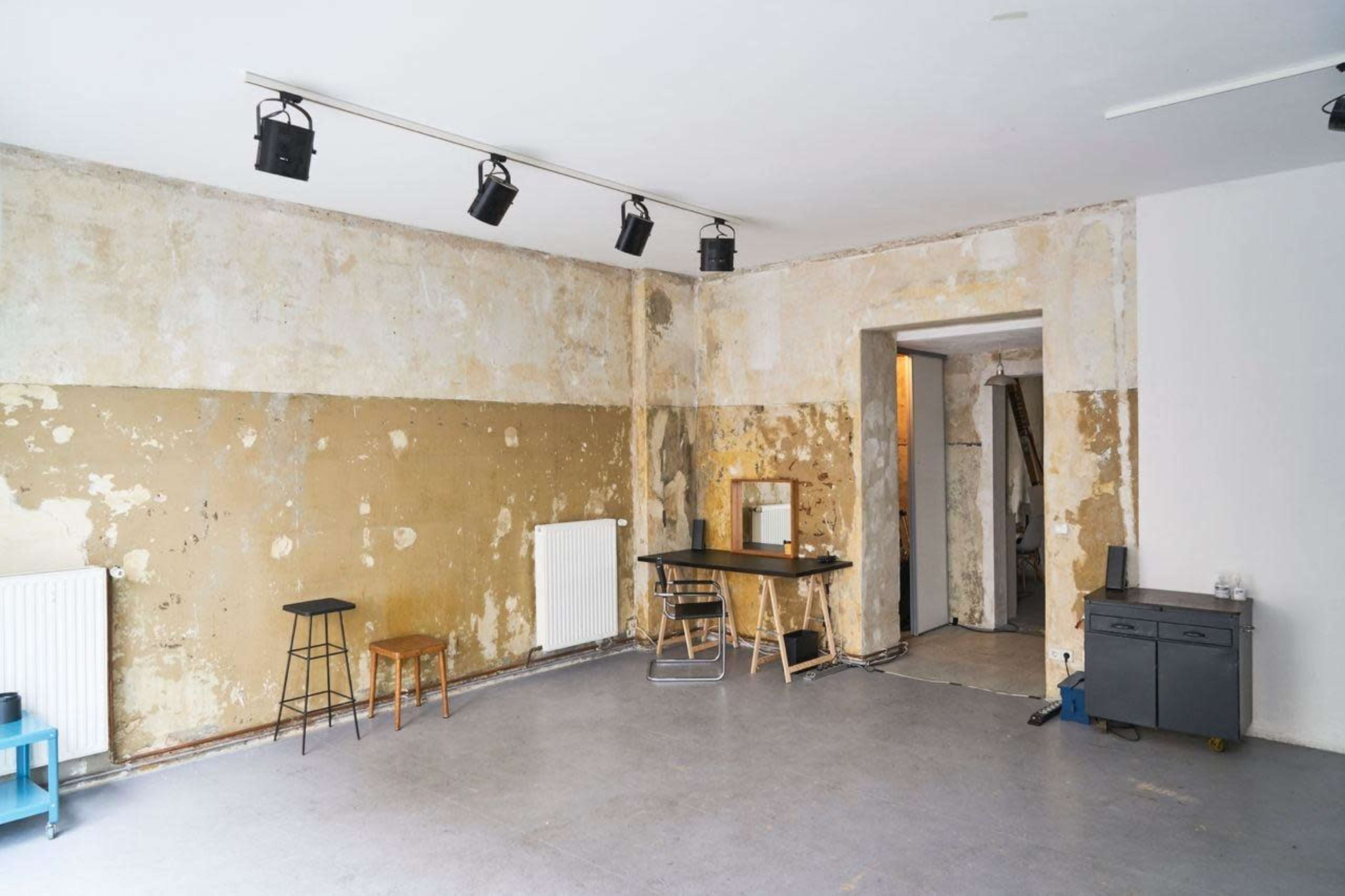 The image shows an empty room with peeling walls, a black table and two chairs, and track lighting on the ceiling.