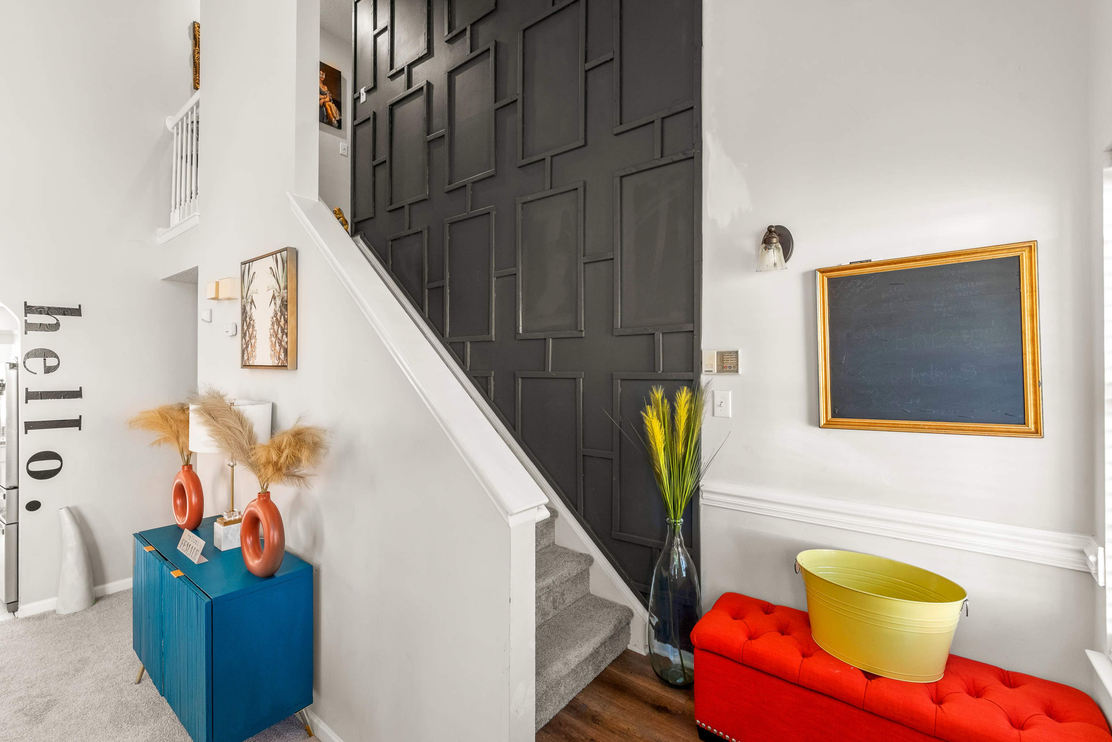 A modern foyer featuring a staircase with a dark accent wall, colorful furniture, and decorative elements like plants and art.