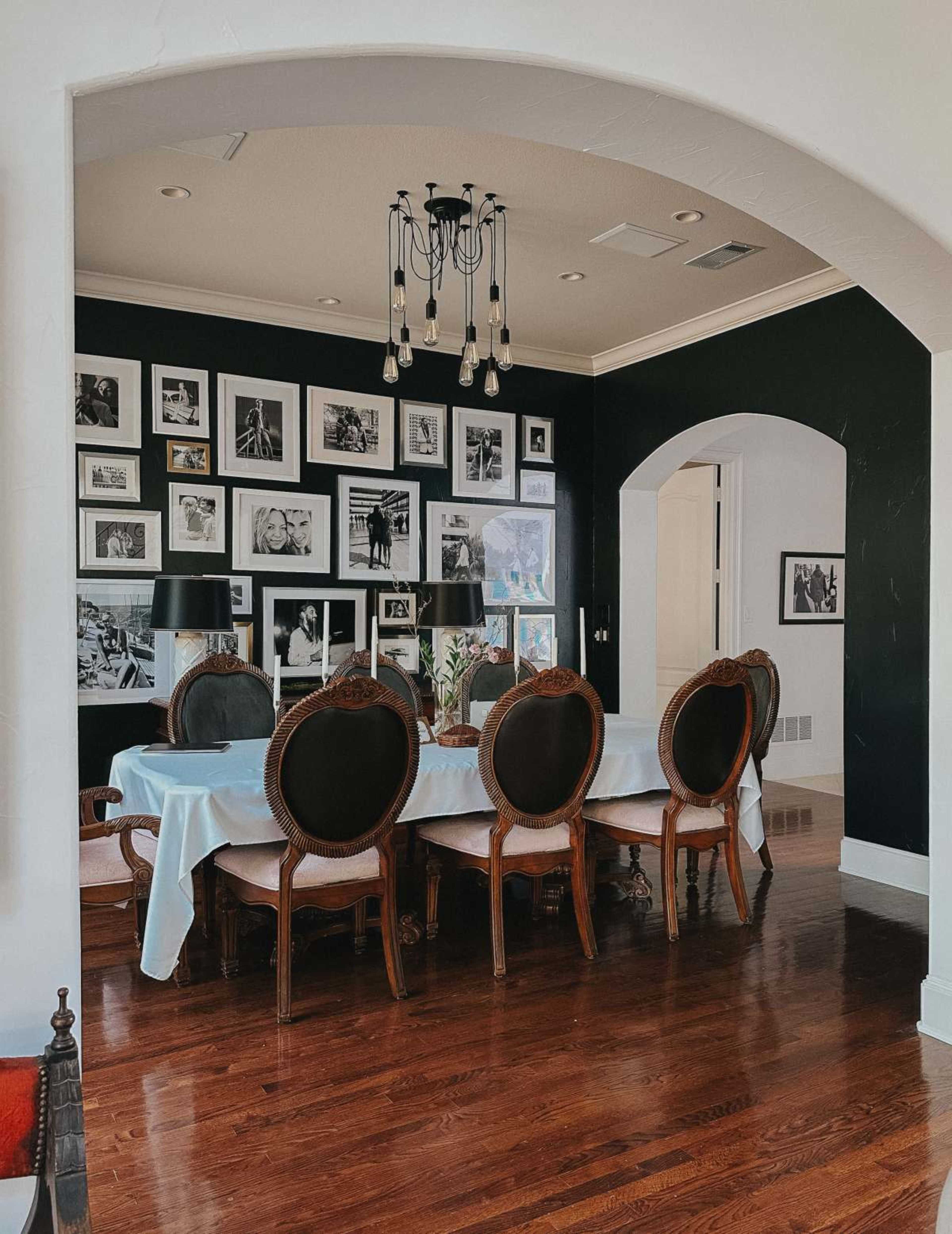 A dining room featuring a long table with ornate chairs, surrounded by framed black-and-white photographs on a dark wall.
